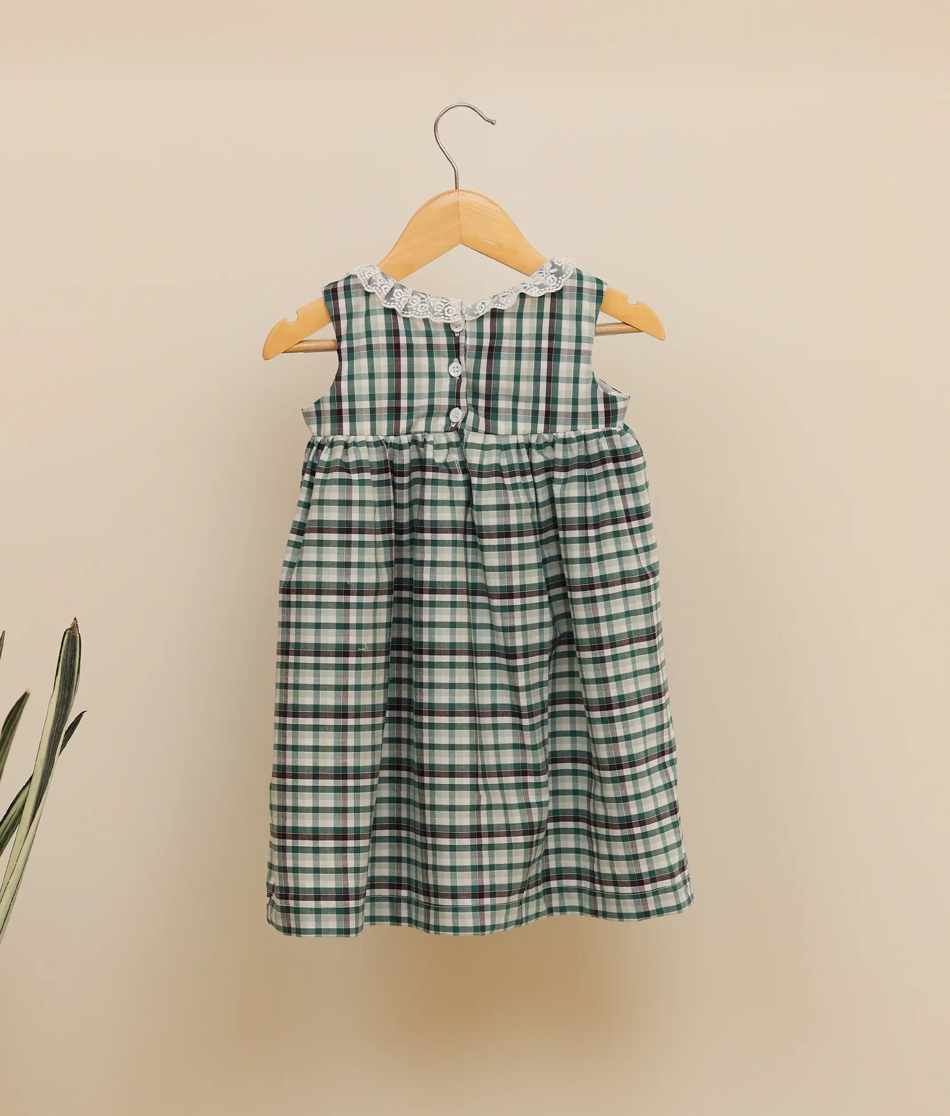 Back view of a green-check-embroidered cotton frock against plain background