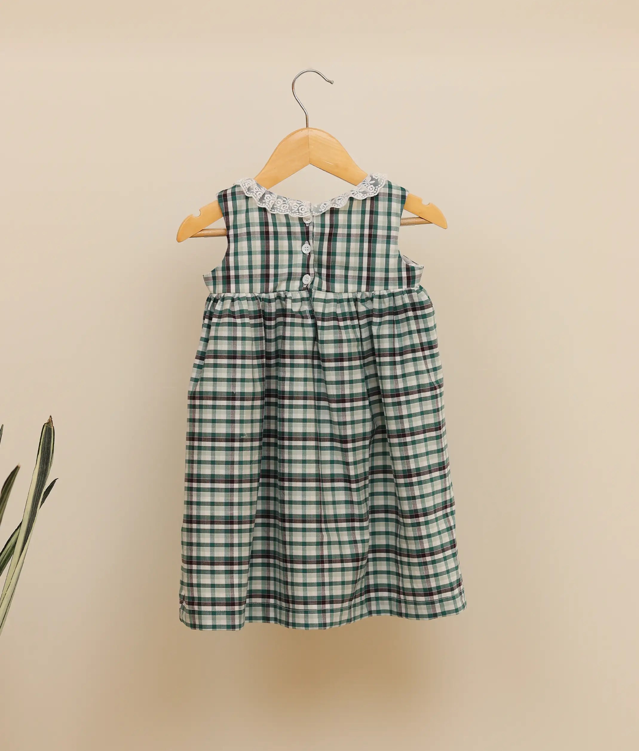Back view of a green-check-embroidered cotton frock against plain background