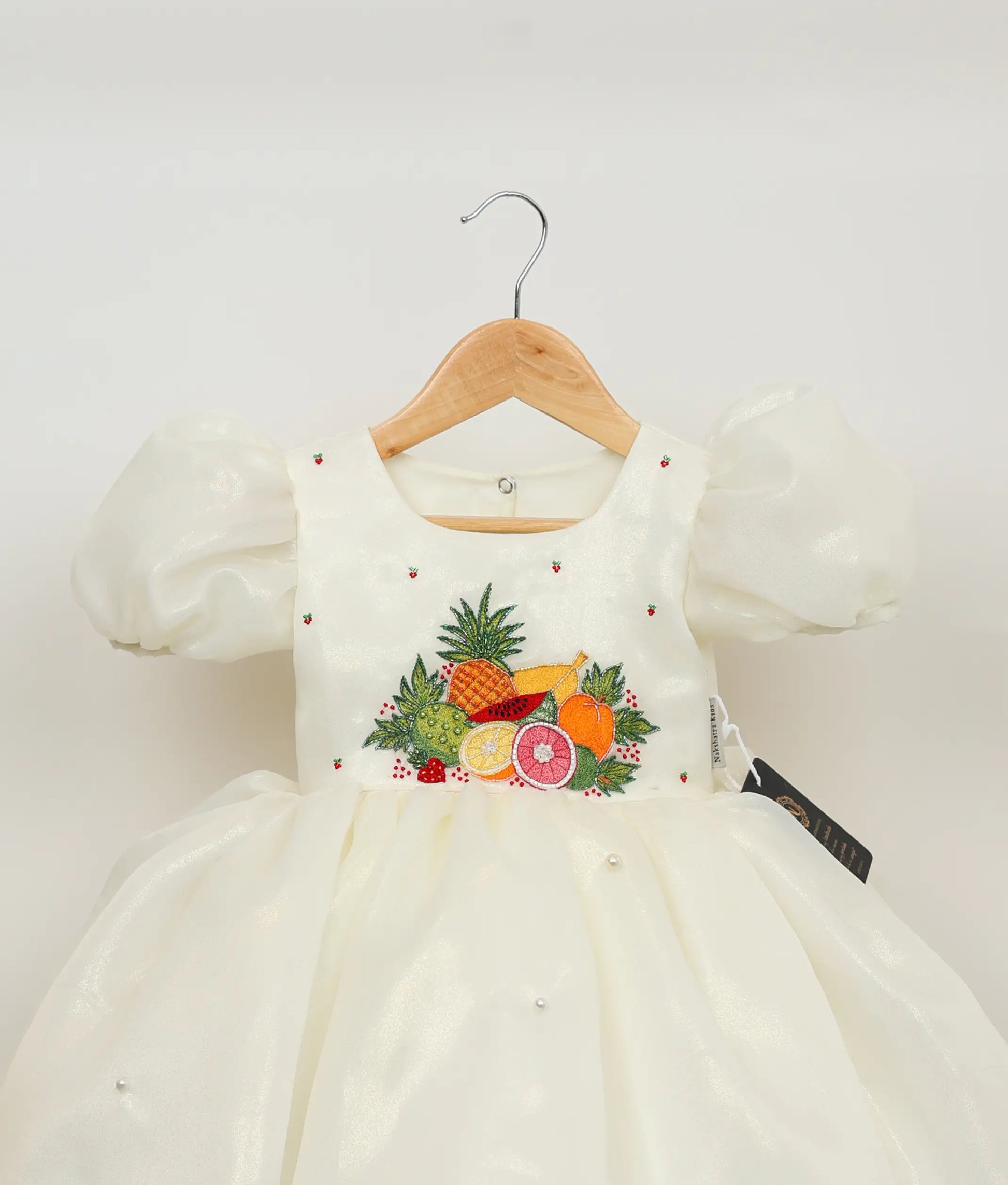 Close view of an off-white plain organza tropical fruit-themed birthday dress against plain background