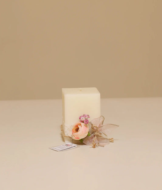 Front view of an off-white square candle with a decorative peach rose, pink sprigs, and a dusty rose ribbon. Perfect for your baby baptism