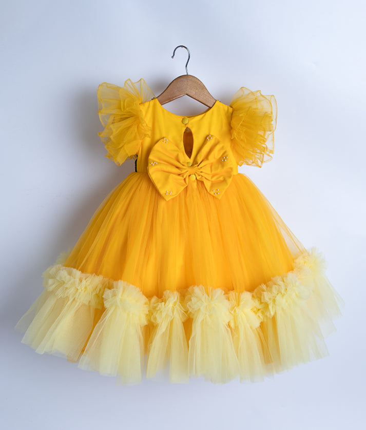 Back view of an yellow tulle net frock displayed on a hanger.