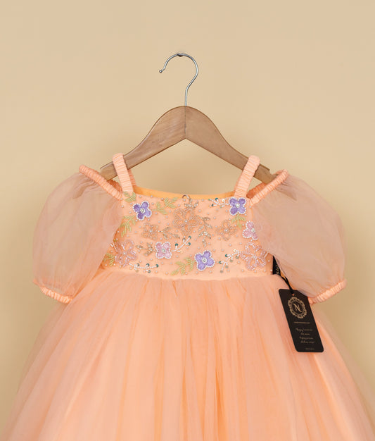 Close view of an peach-colored dress with floral embellishments on a hanger against a beige background.