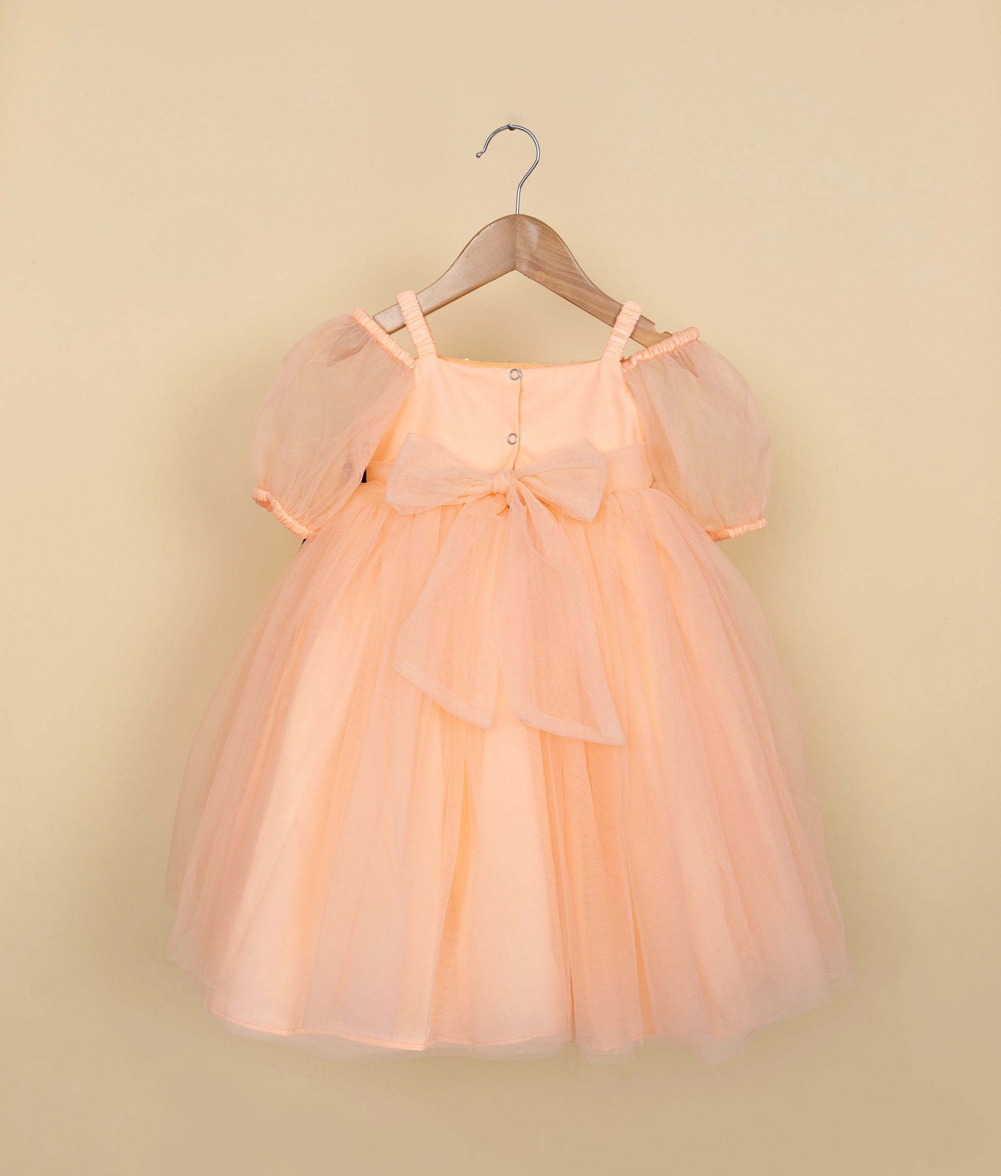 Back view of an peach-colored tulle dress on a hanger against a beige background.