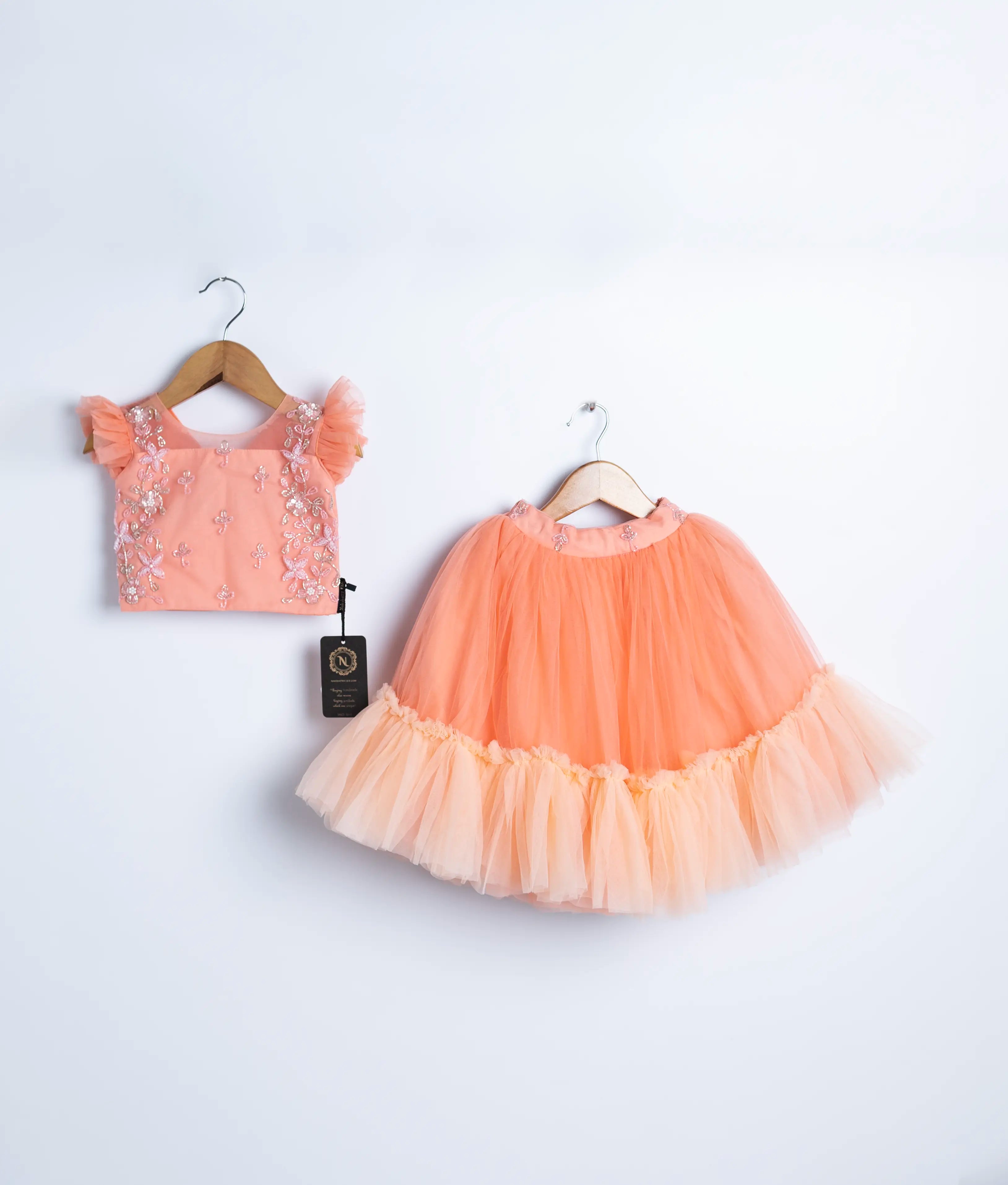 Peach tulle net handworked top and skirt is displayed on a hanger. 