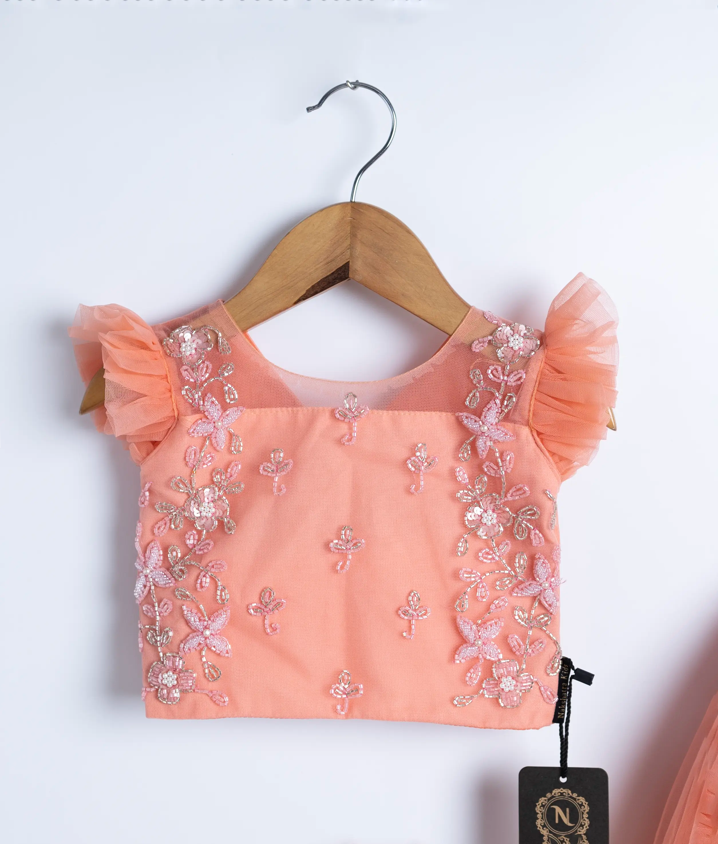 Close view of an peach tulle net handworked top and skirt is displayed on a hanger. 