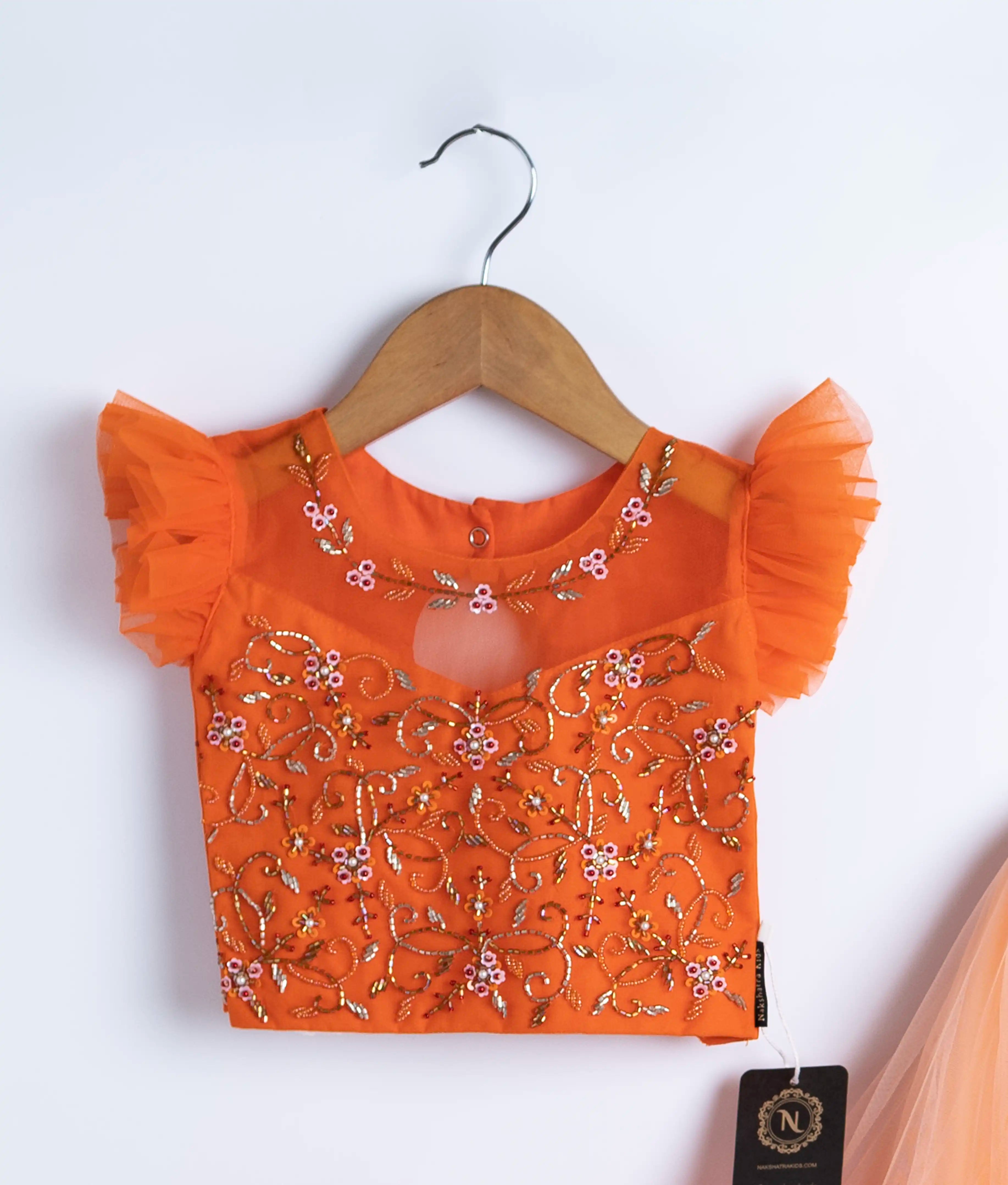 Close view of an orange handworked crop top displayed on hangers against a white background.