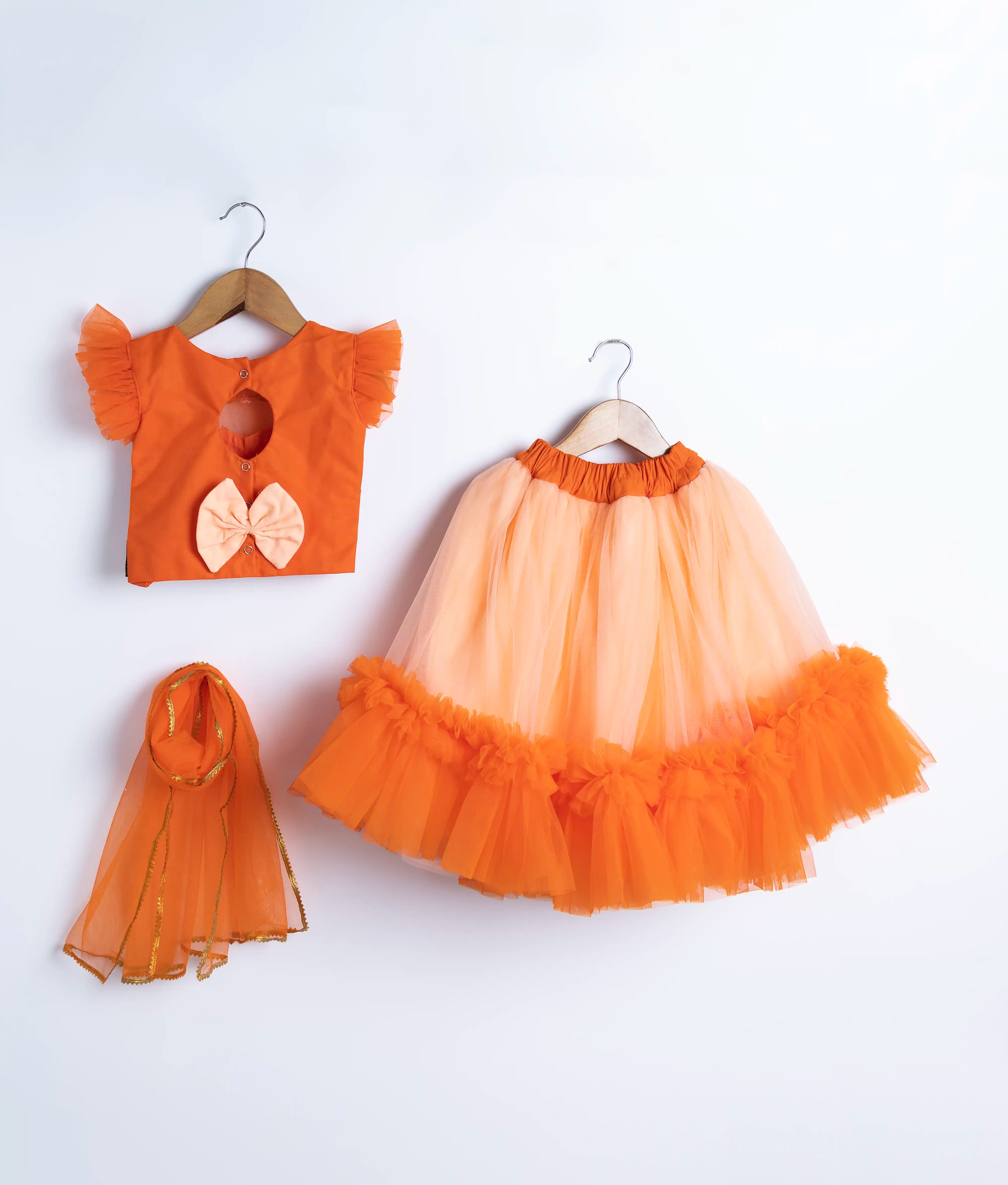 Back view of an orange handworked crop top peach skirt and a matching orange dupatta displayed on hangers against a white background.