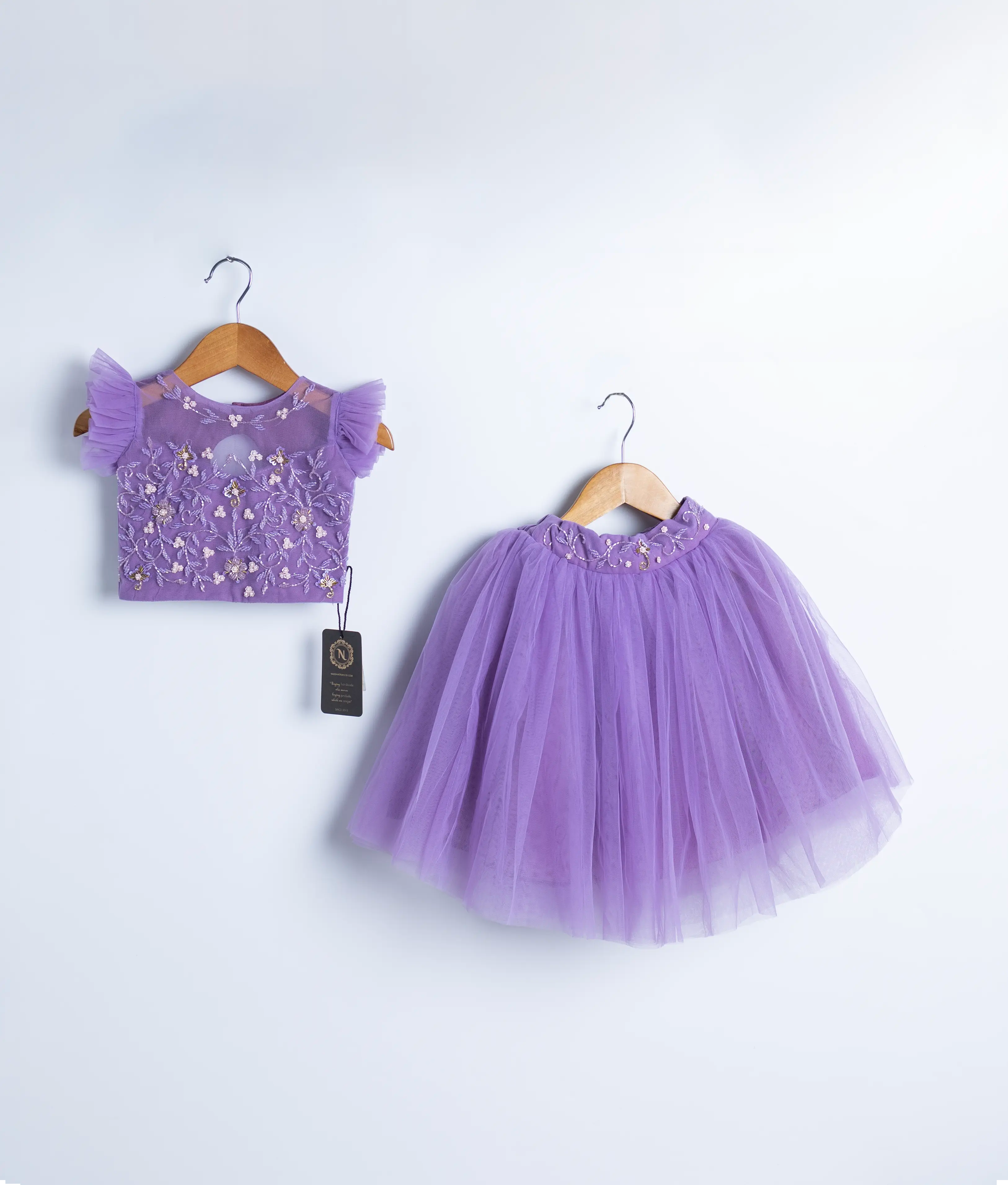 A lavender crop top and full-length skirt on wooden hangers against a white background.