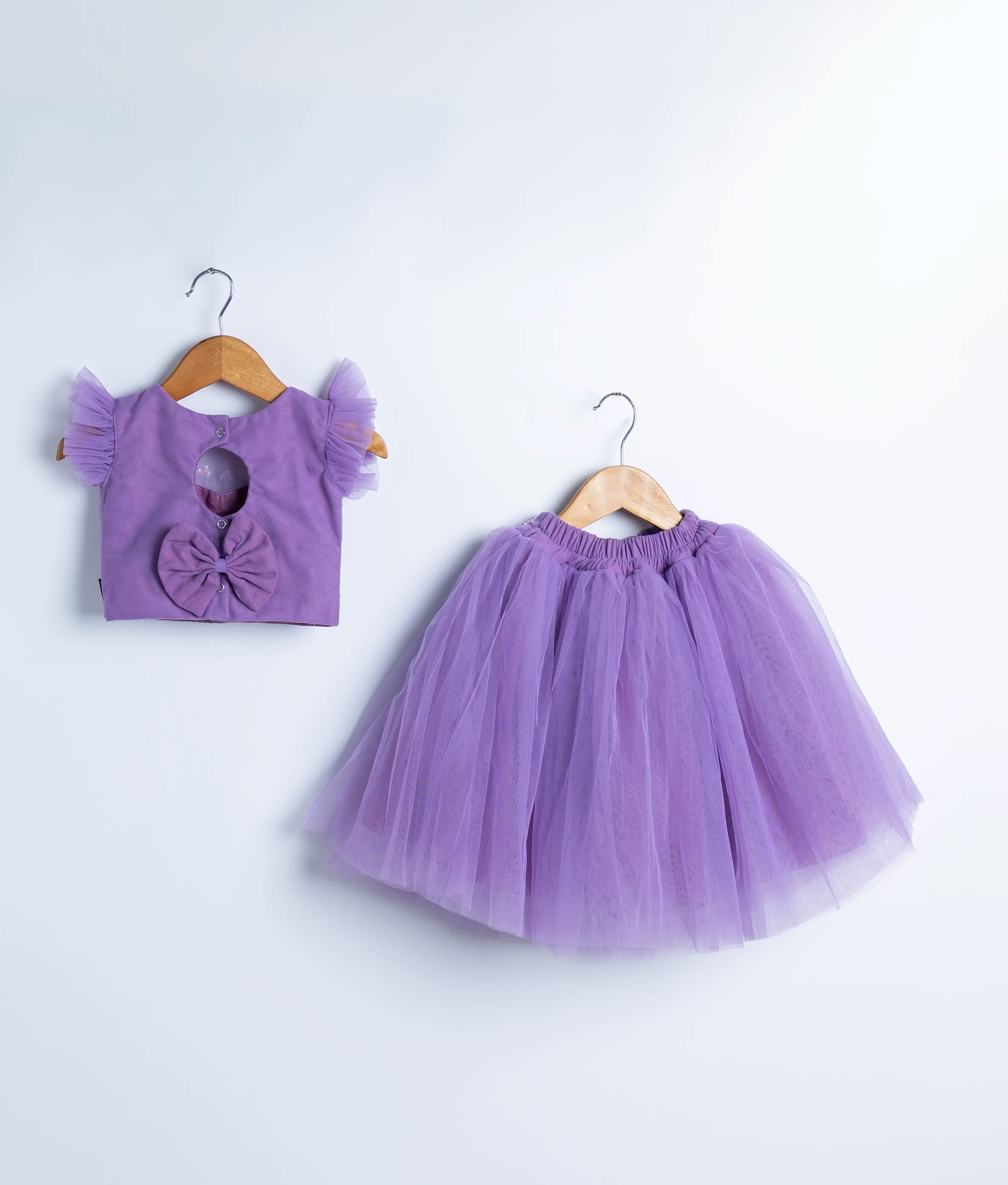 Back view of an lavender crop top and full-length skirt on wooden hangers against a white background.
