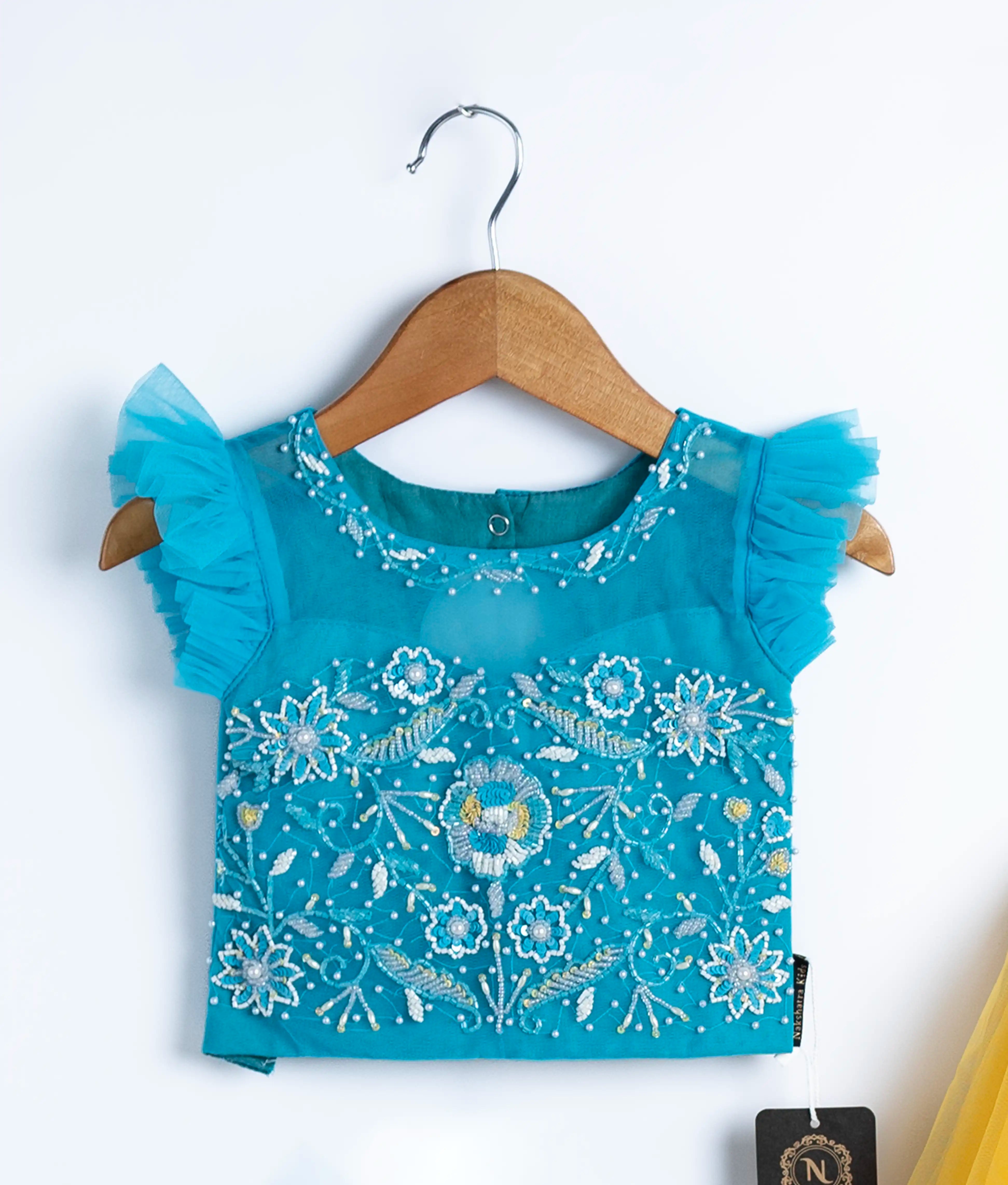 Close view of an blue tulle net handworked crop top displayed on a hanger.