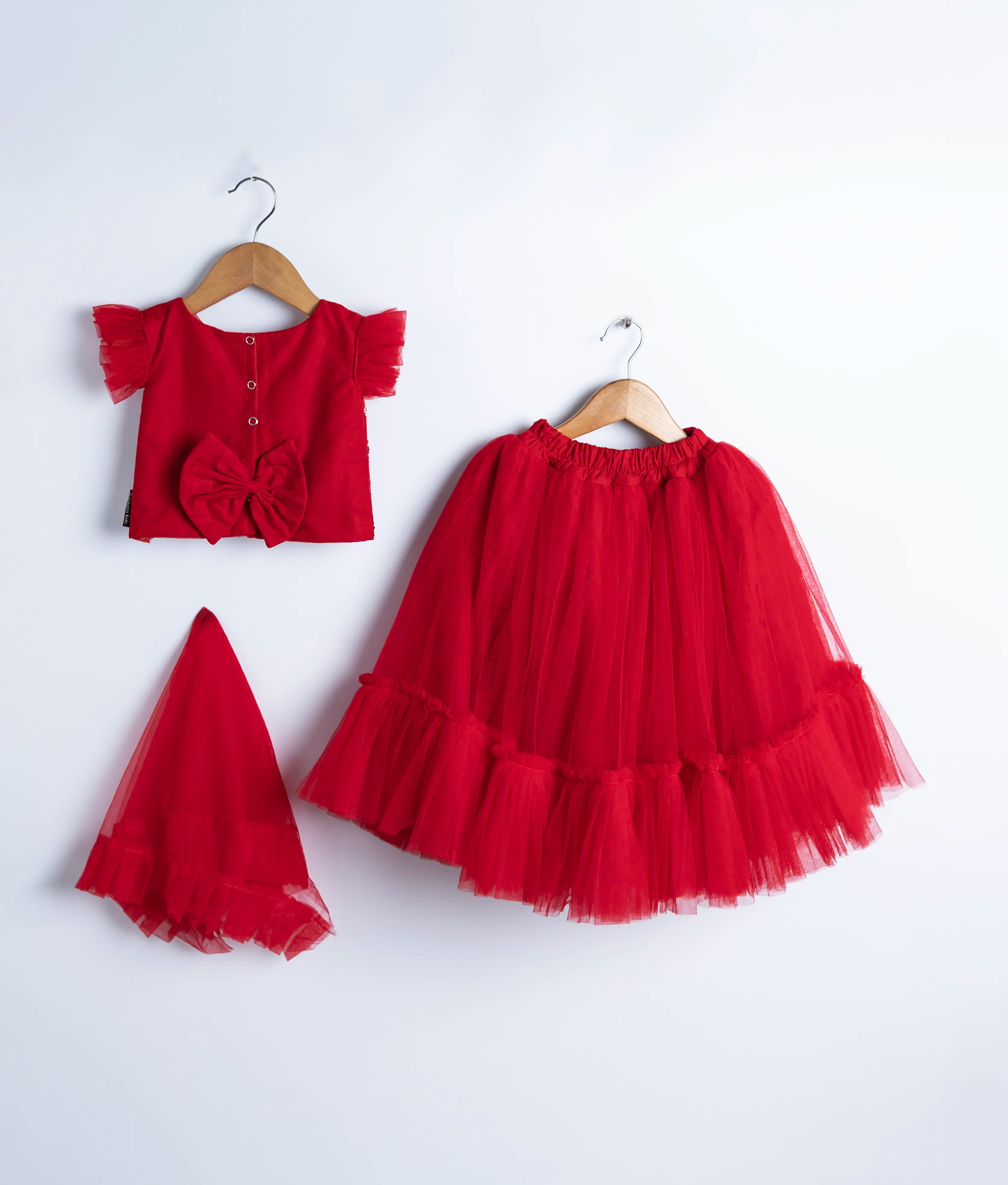 Back view of an red tulle net handworked crop top and skirt is displayed on hangers against a white background.