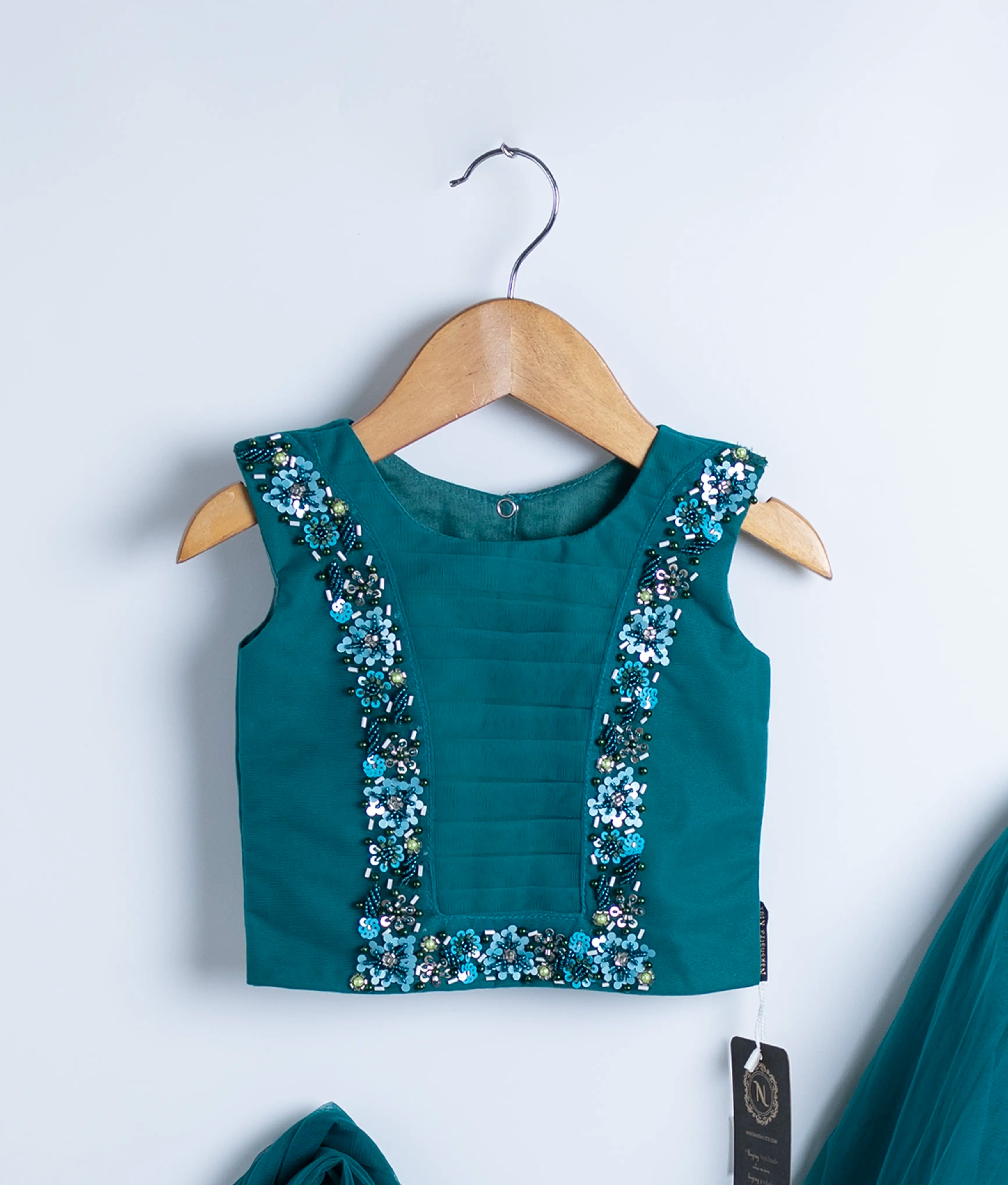 Close view of an peacock blue crop top displayed on hangers against a white background.
