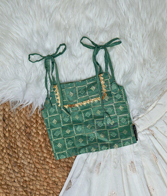 Close view of traditional Indian ethnic wear for girls featuring a white embroidered skirt with leaf motifs and a green block-printed blouse with golden detailing, displayed on a white furry mat.