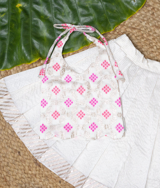 Close view of a stylish festive outfit featuring a white embroidered halter-neck top with pink and gold sequin work, paired with a pleated off-white skirt with subtle golden detailing—perfect for traditional celebrations.