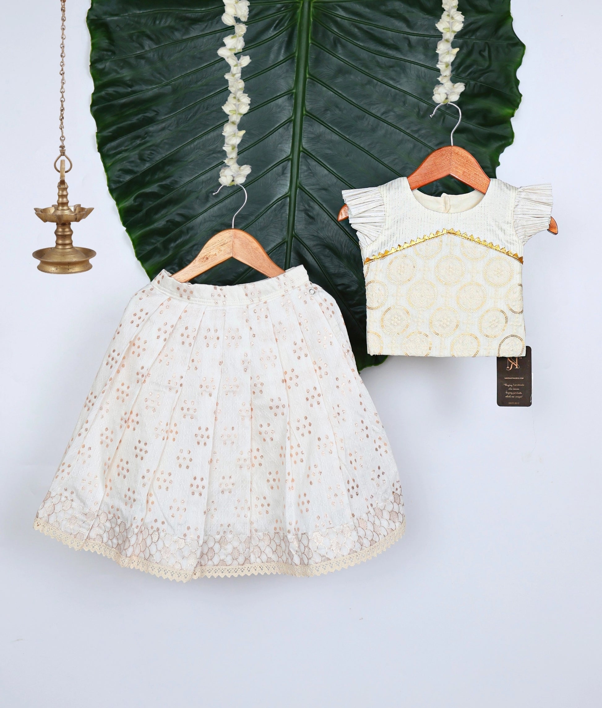 White lace dress and top on hangers with decorative leaves in the background.