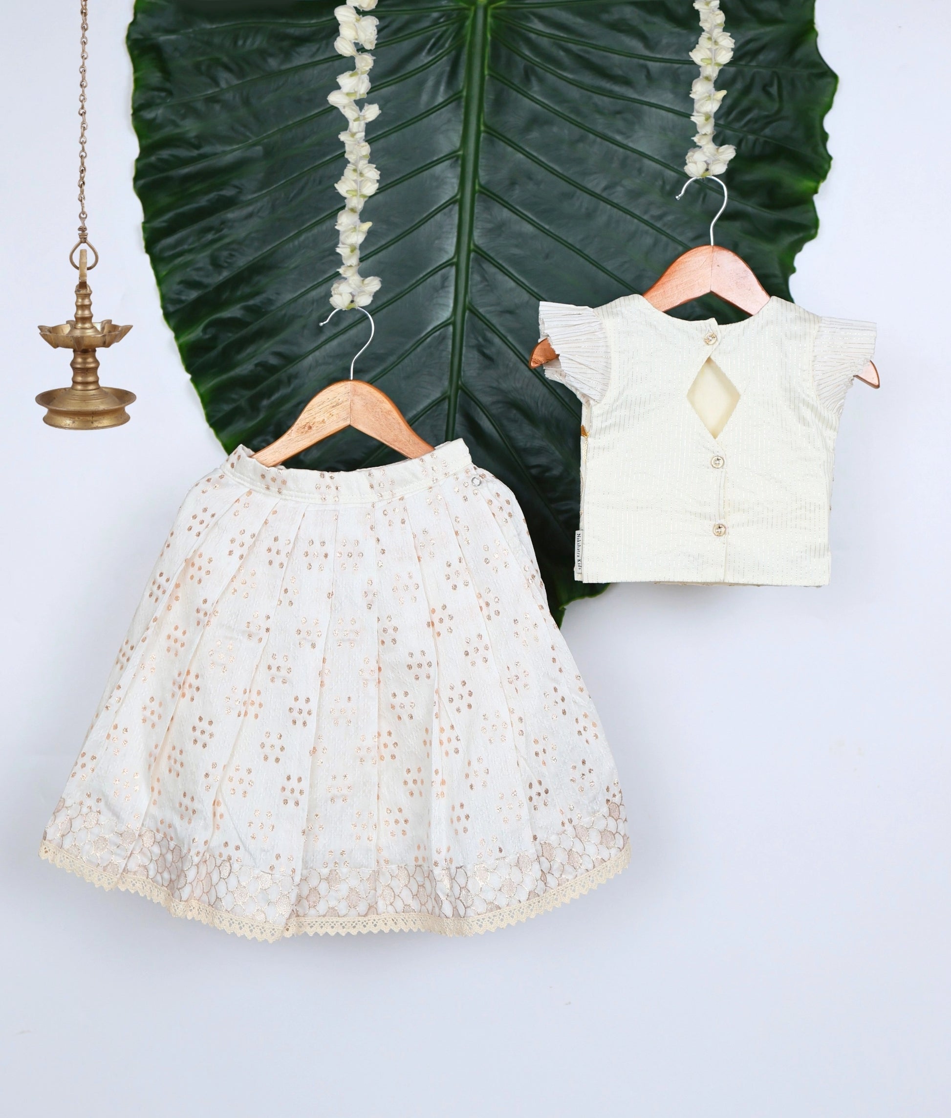 White lace skirt and blouse on hangers against a leafy background.
