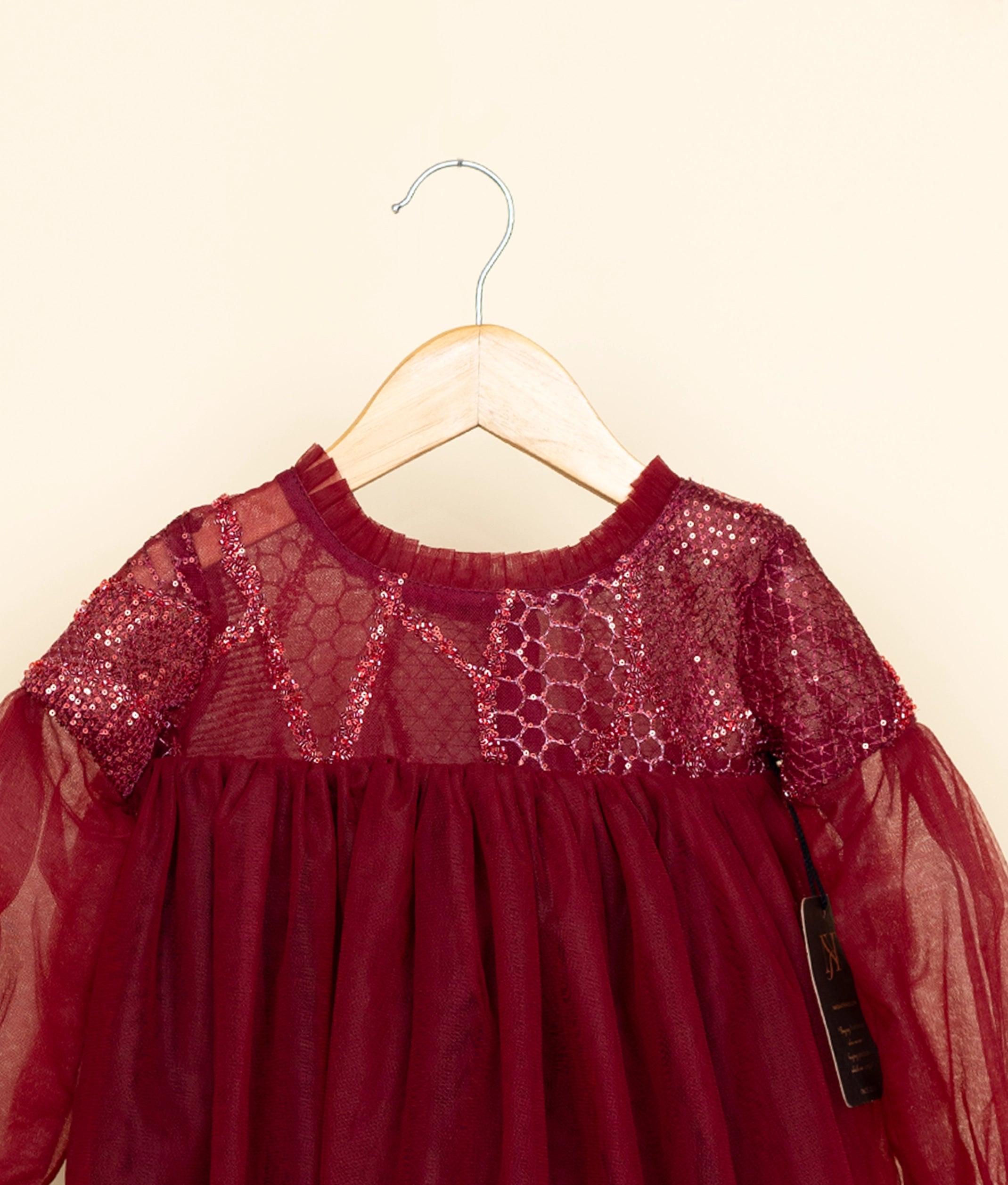 Red dress with sequin details on a hanger against a beige background