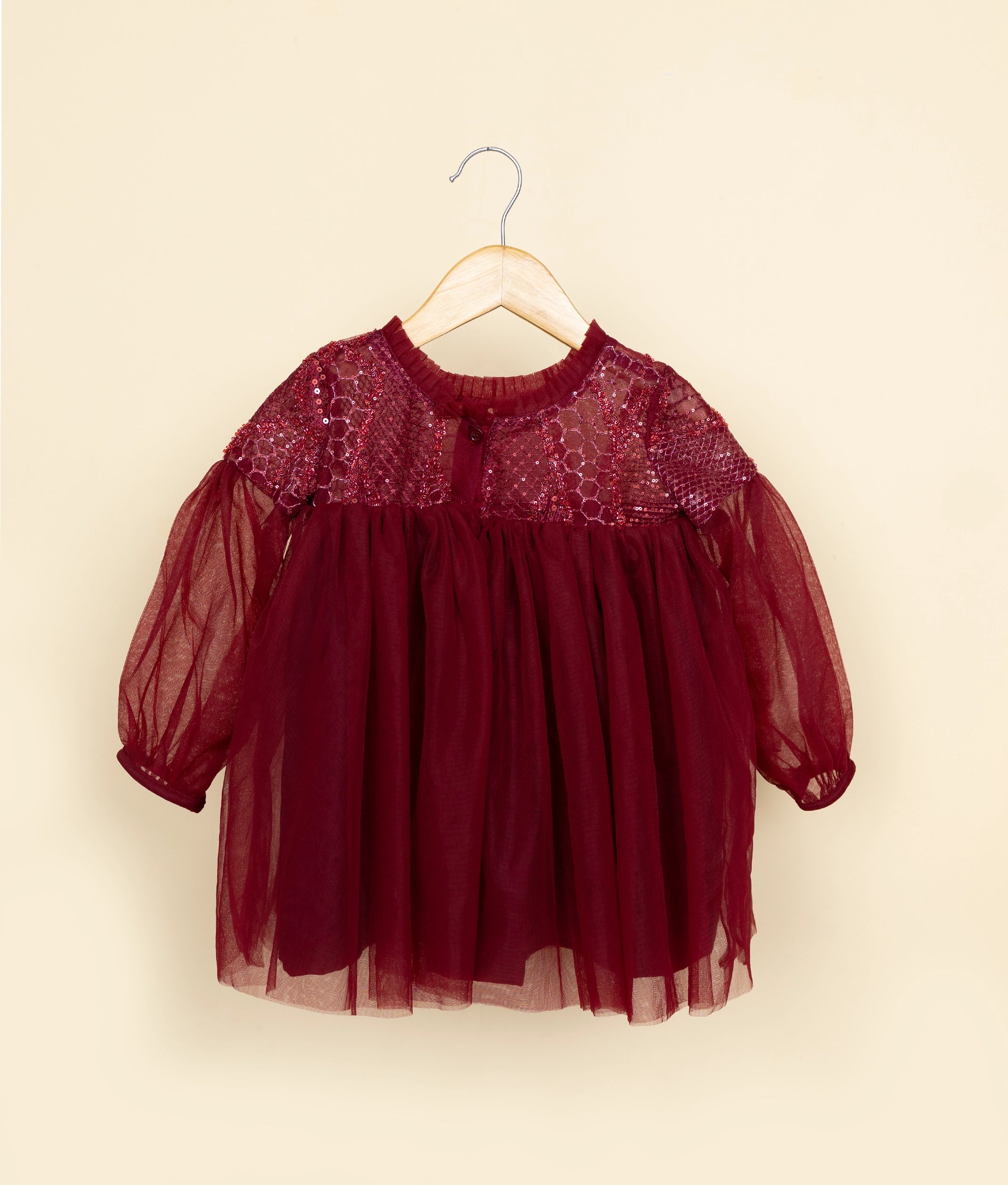 Red dress with sheer sleeves on a hanger against a beige background