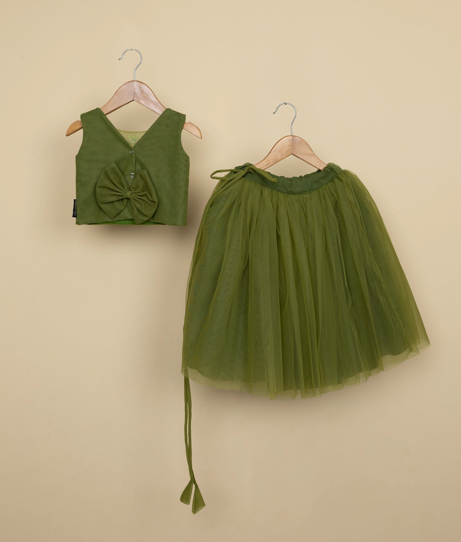 Back view of an olive green floral tulle net top and skirt on hangers against a beige wall background.