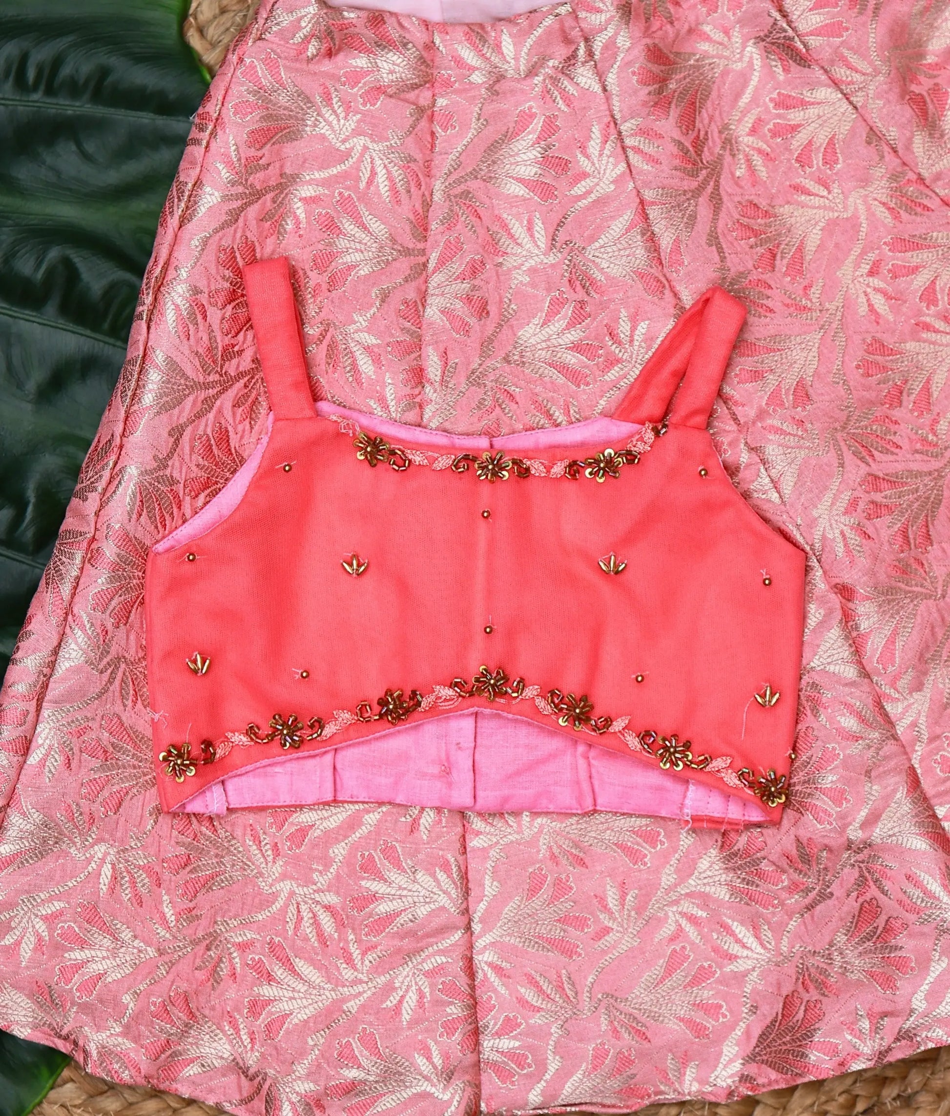 Close view of a stylish pink kids lehenga set with a floral brocade skirt and an embellished sleeveless top.