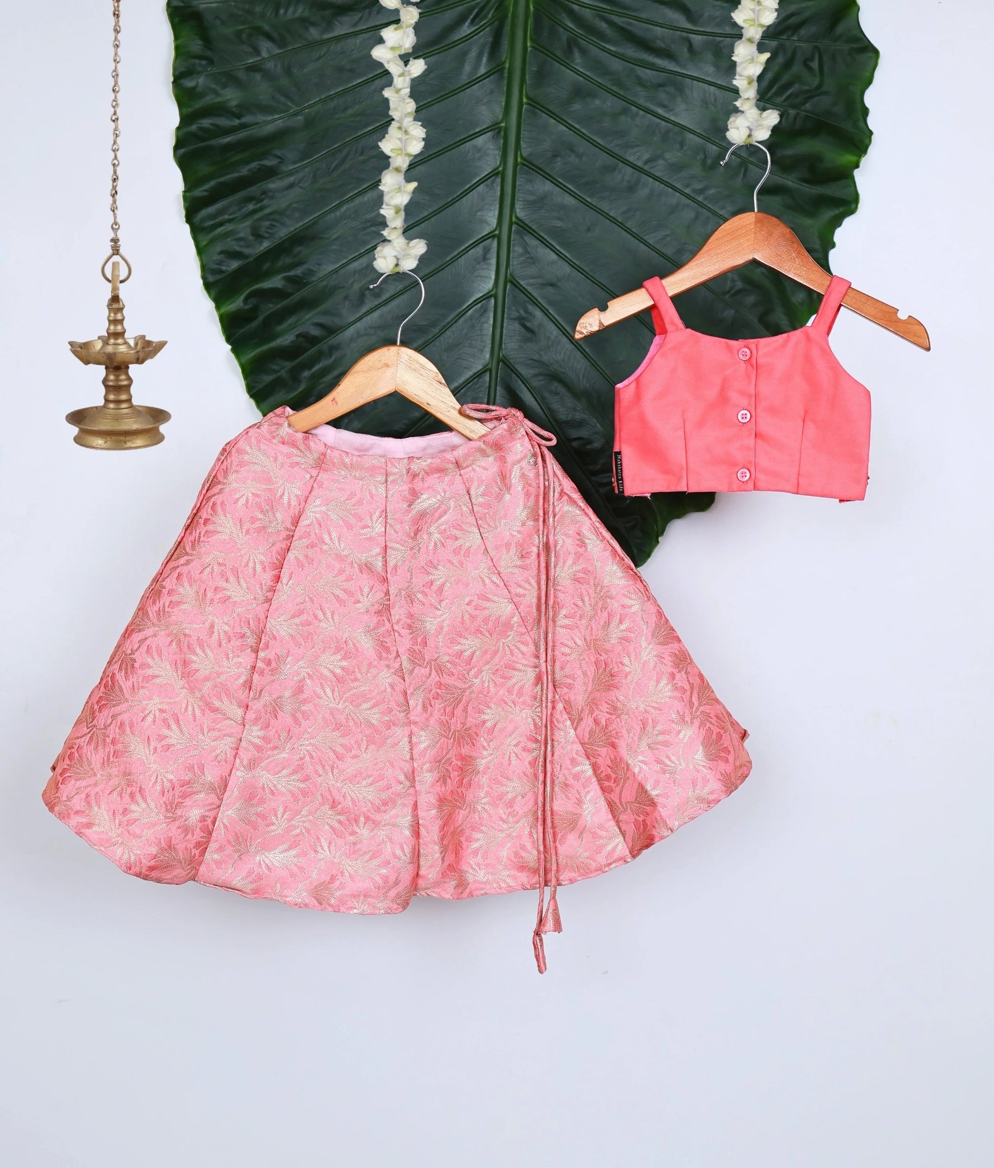 Back view of a stylish pink kids lehenga set with a floral brocade skirt and an embellished sleeveless top.