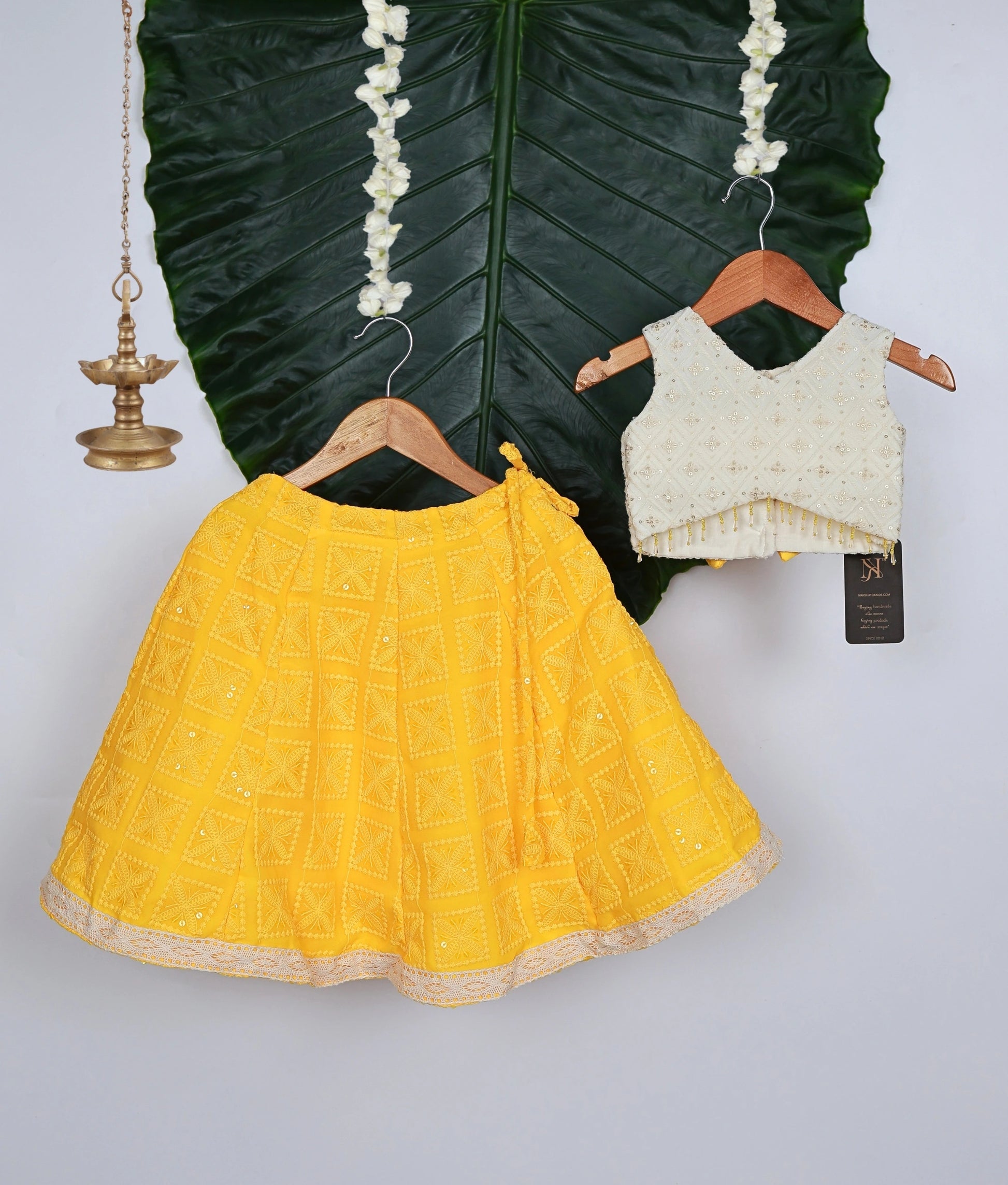 Traditional baby girl outfit with a yellow georgette lehenga and an off-white work-material embellished sleeveless top.