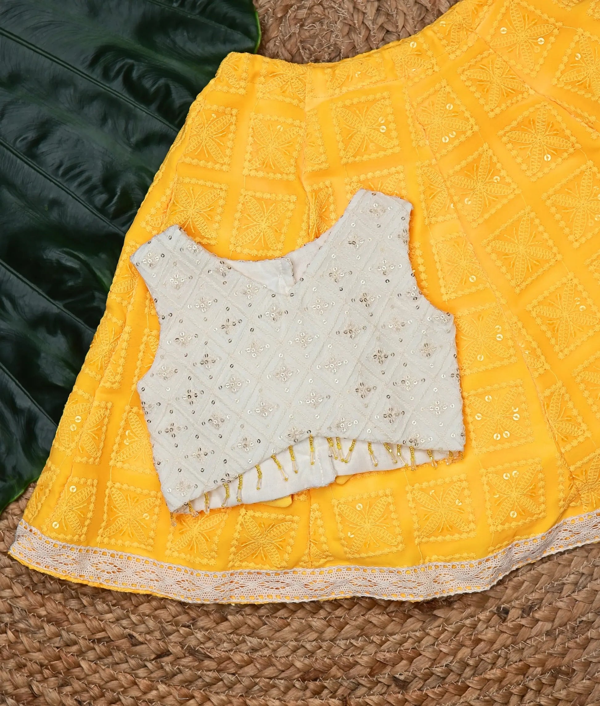 Close view of traditional baby girl outfit with yellow georgette lehenga and off-white work-material embellished sleeveless top.