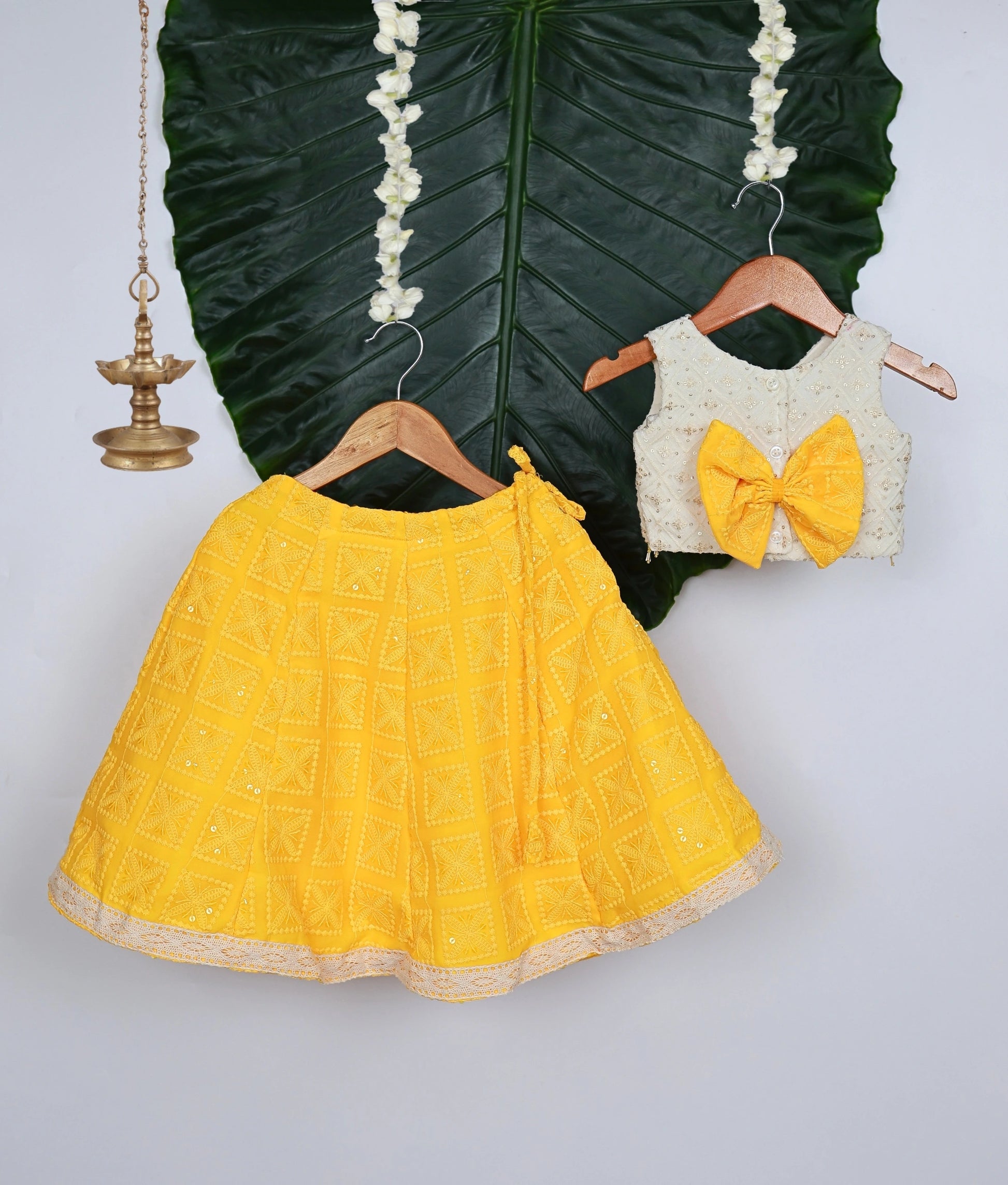 Back view of a traditional baby girl outfit with a yellow georgette lehenga and an off-white work-material embellished sleeveless top.