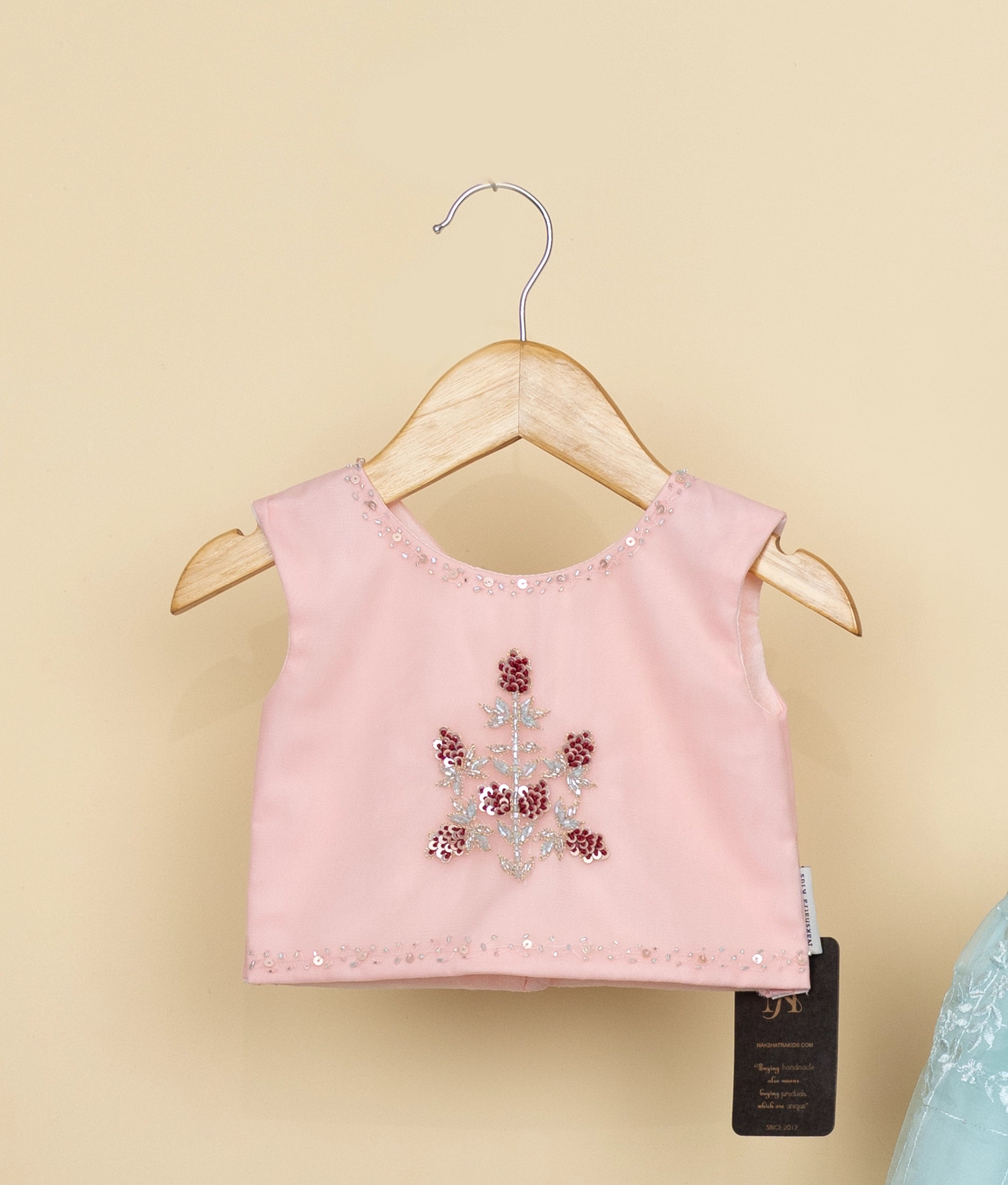 Pink children's top with floral embellishments on a hanger against a beige background
