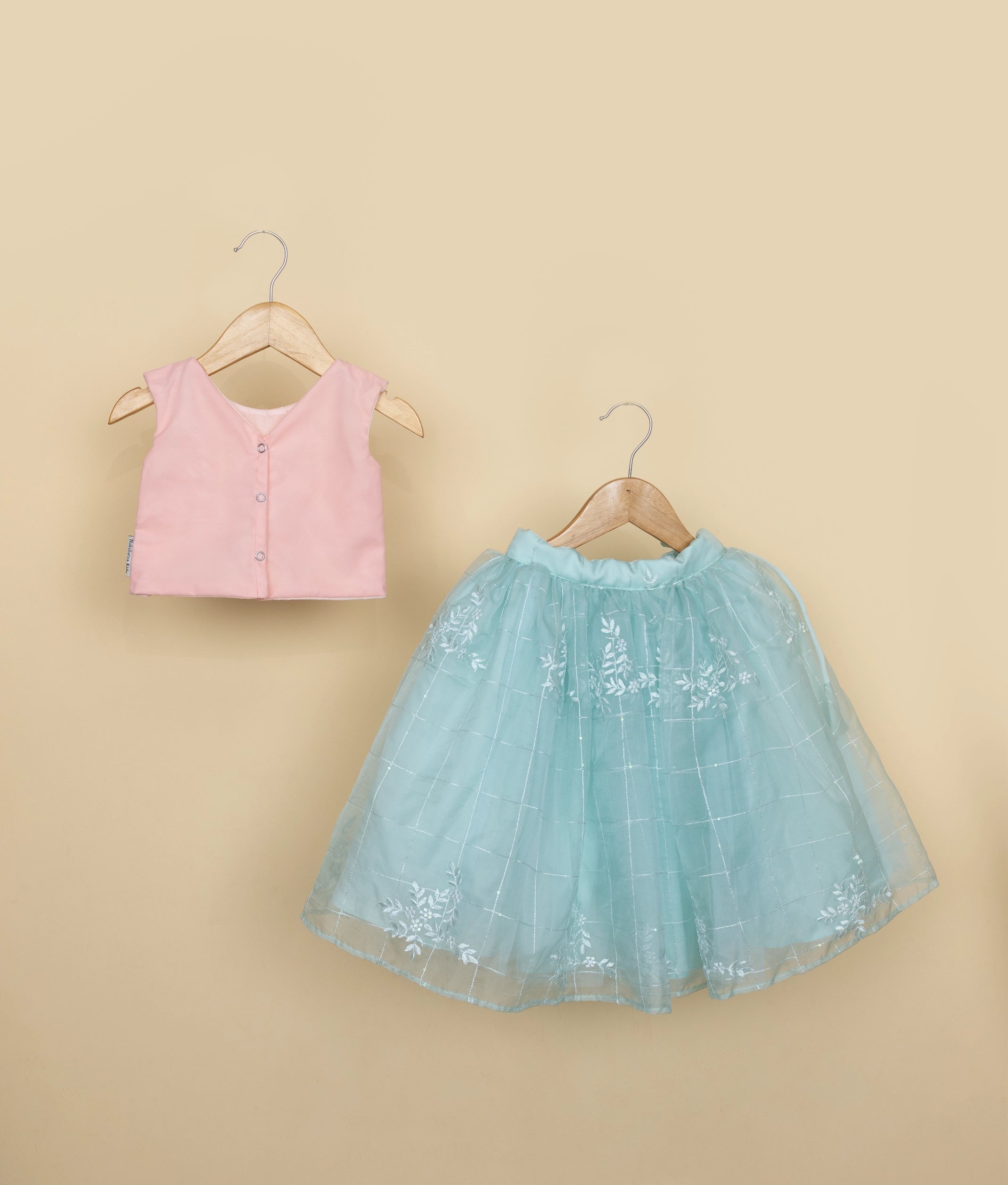 Back view of a pink sleeveless top and blue tulle skirt with floral embroidery on a beige background.