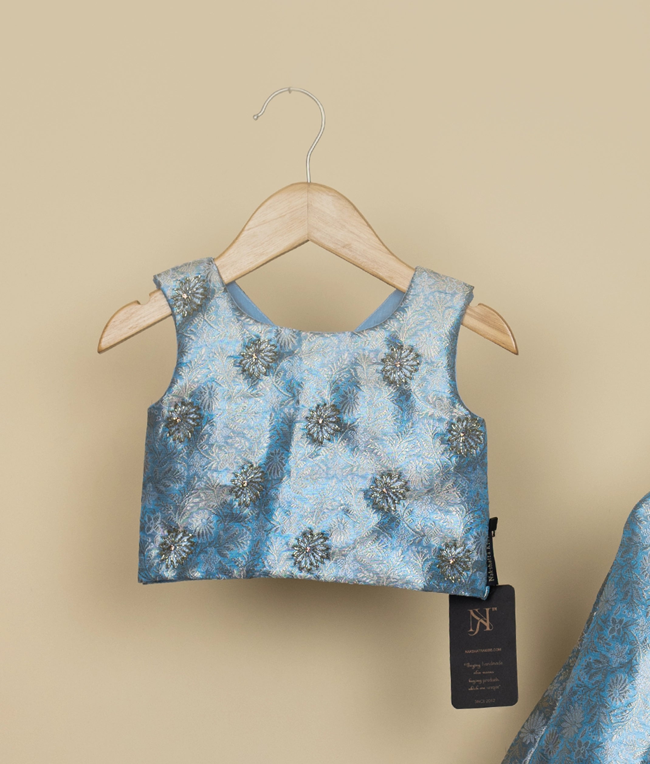 Sky blue handworked floral-patterned top on a hanger against a beige background.