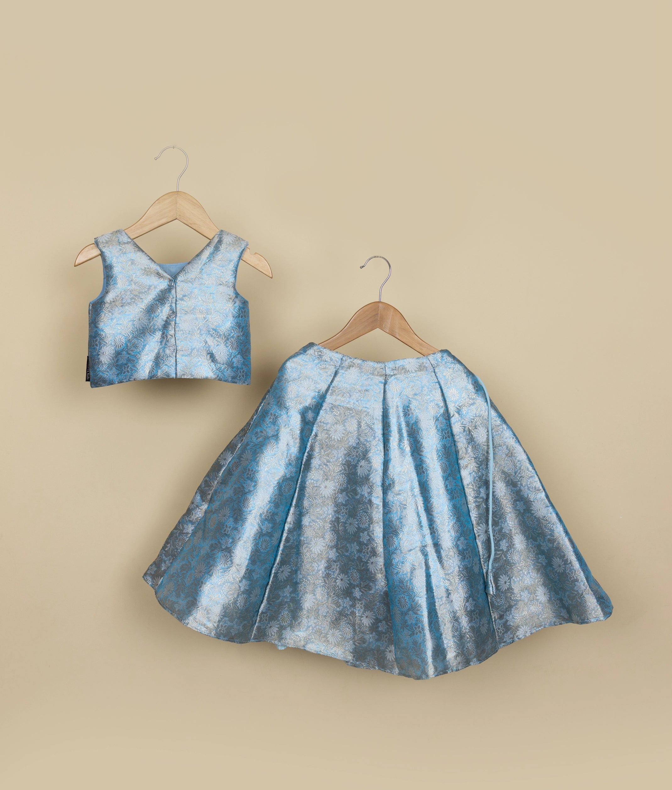 Back view of a sky blue Banarasi top and skirt set on hangers against a beige background.