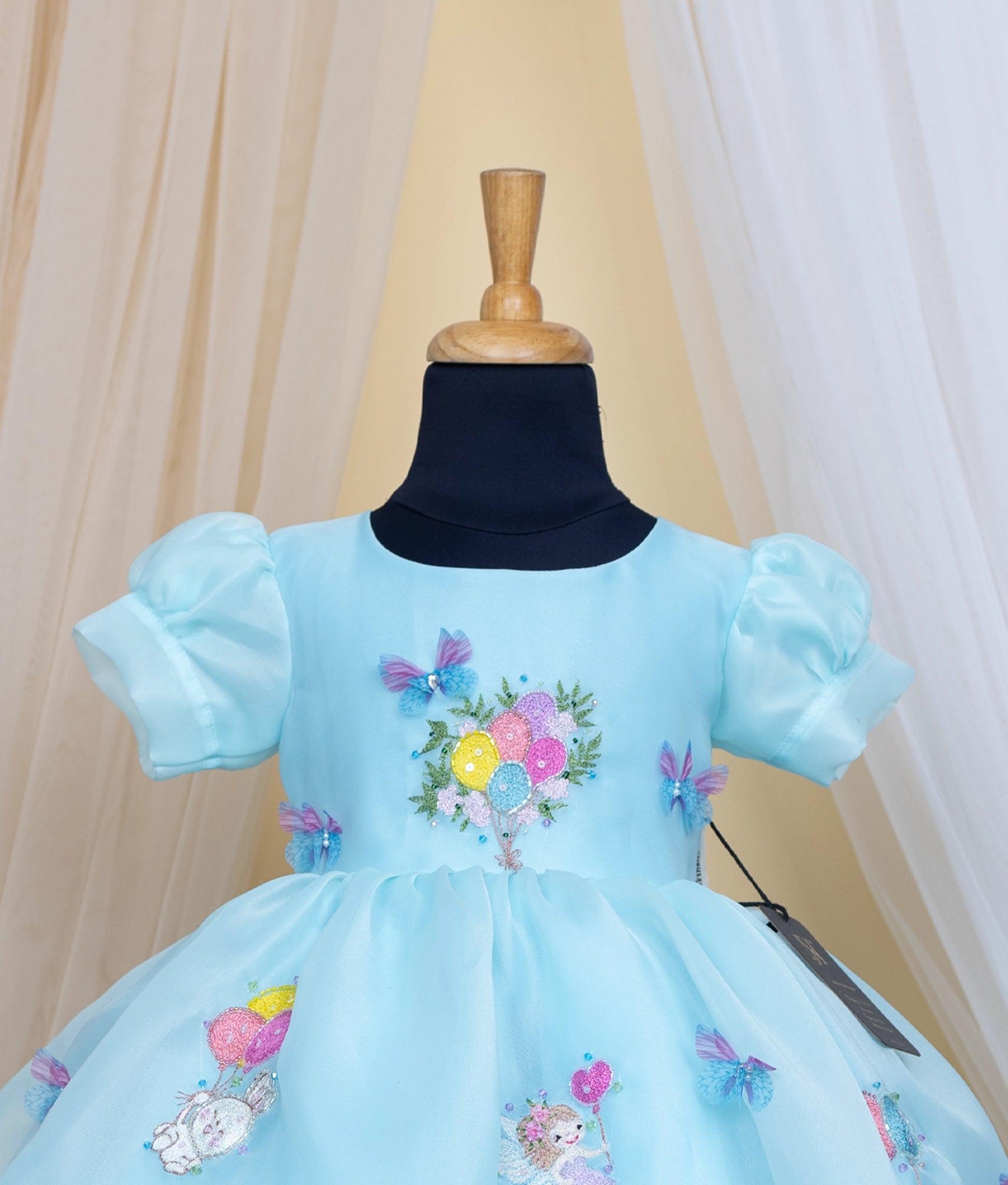 Close view of an sky blue dress with baloon theme on a mannequin against a beige curtain background.