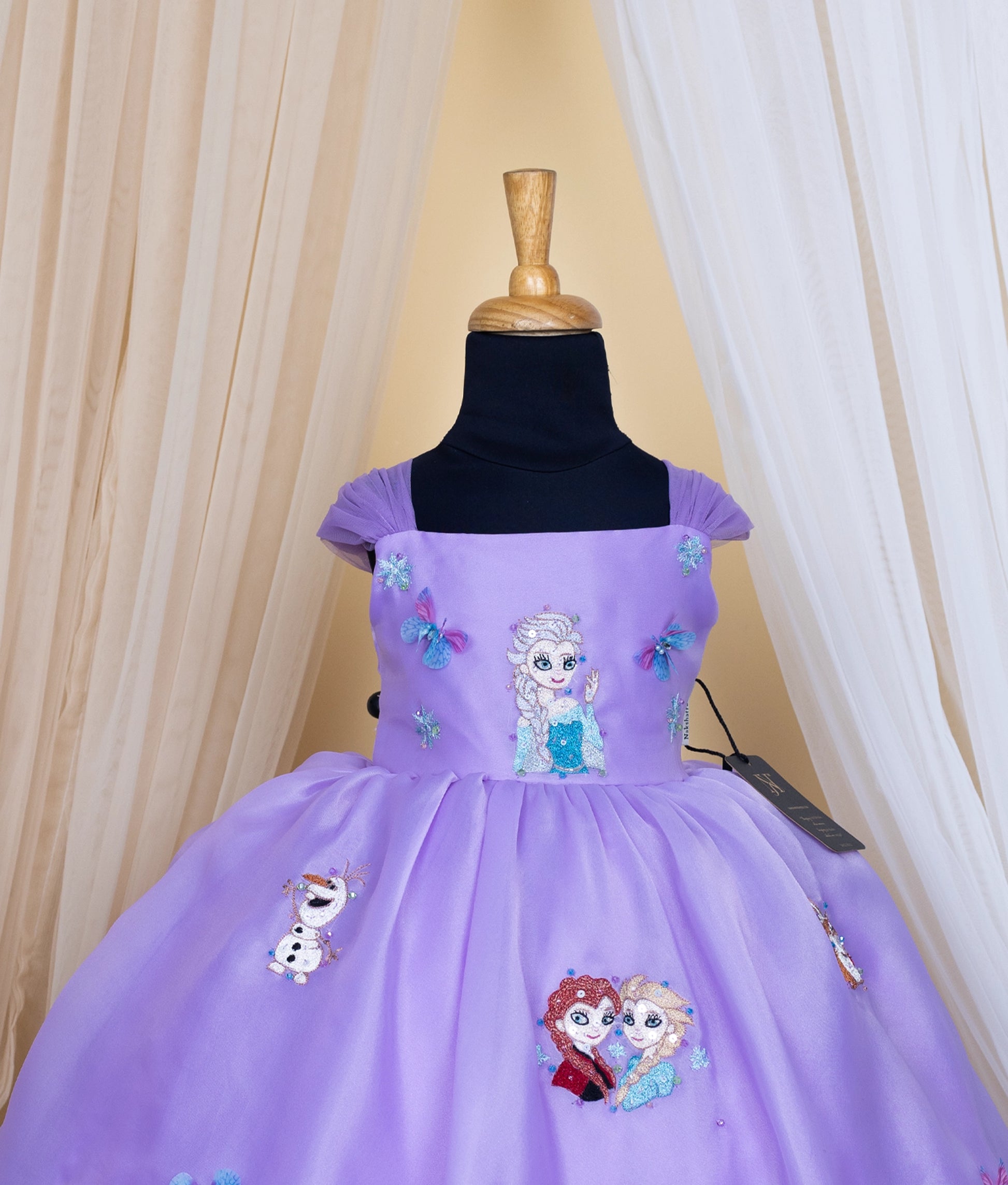 Close view of lavender elsa theme with character embroidery on a mannequin against a beige curtain background.