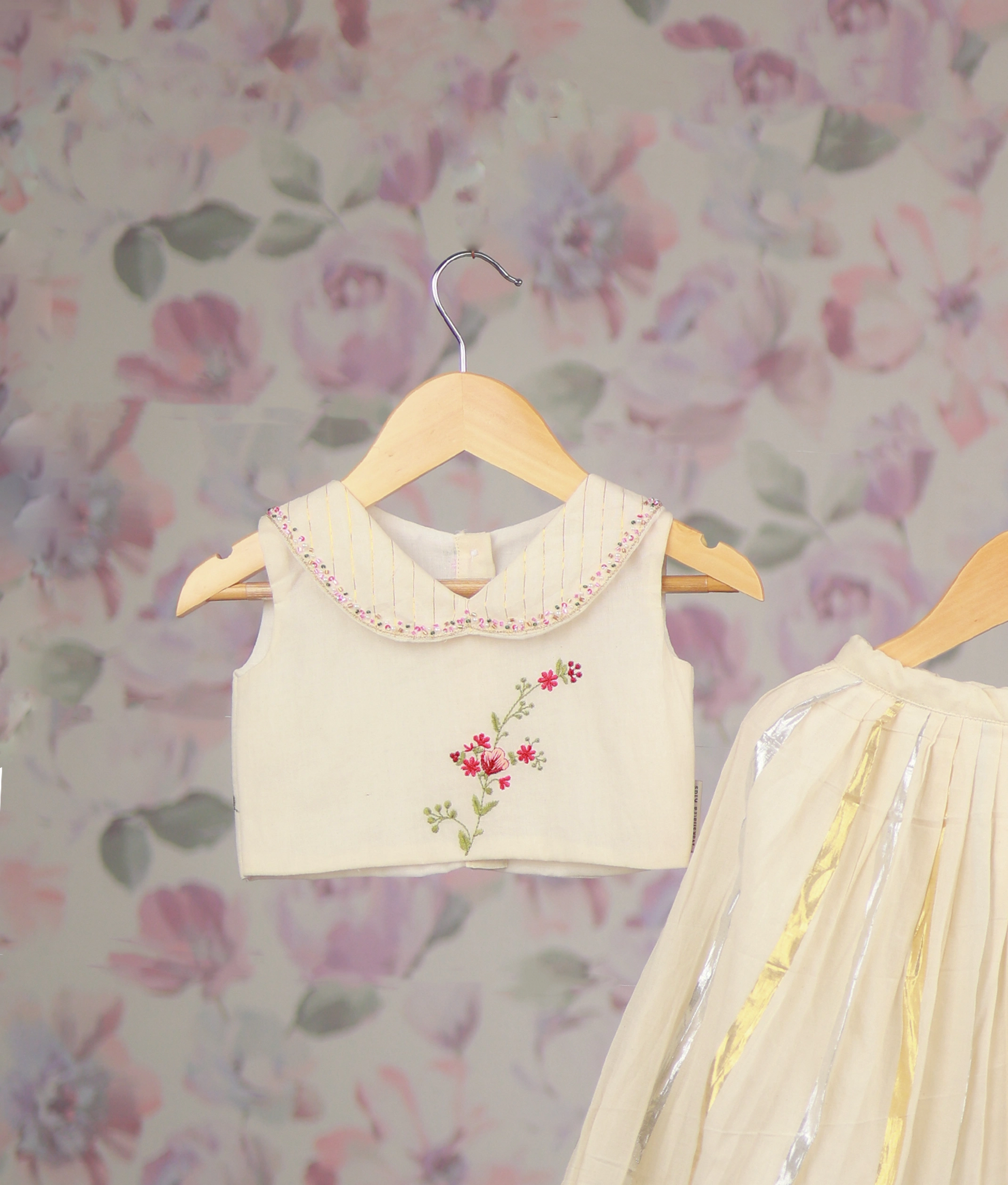 Close view of an off-white baby girl's festive skirt set with a floral embroidery top and a golden Kasav line skirt.