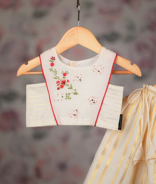Close view of an off-white and golden baby girl skirt with embroidery top, displayed on hangers.