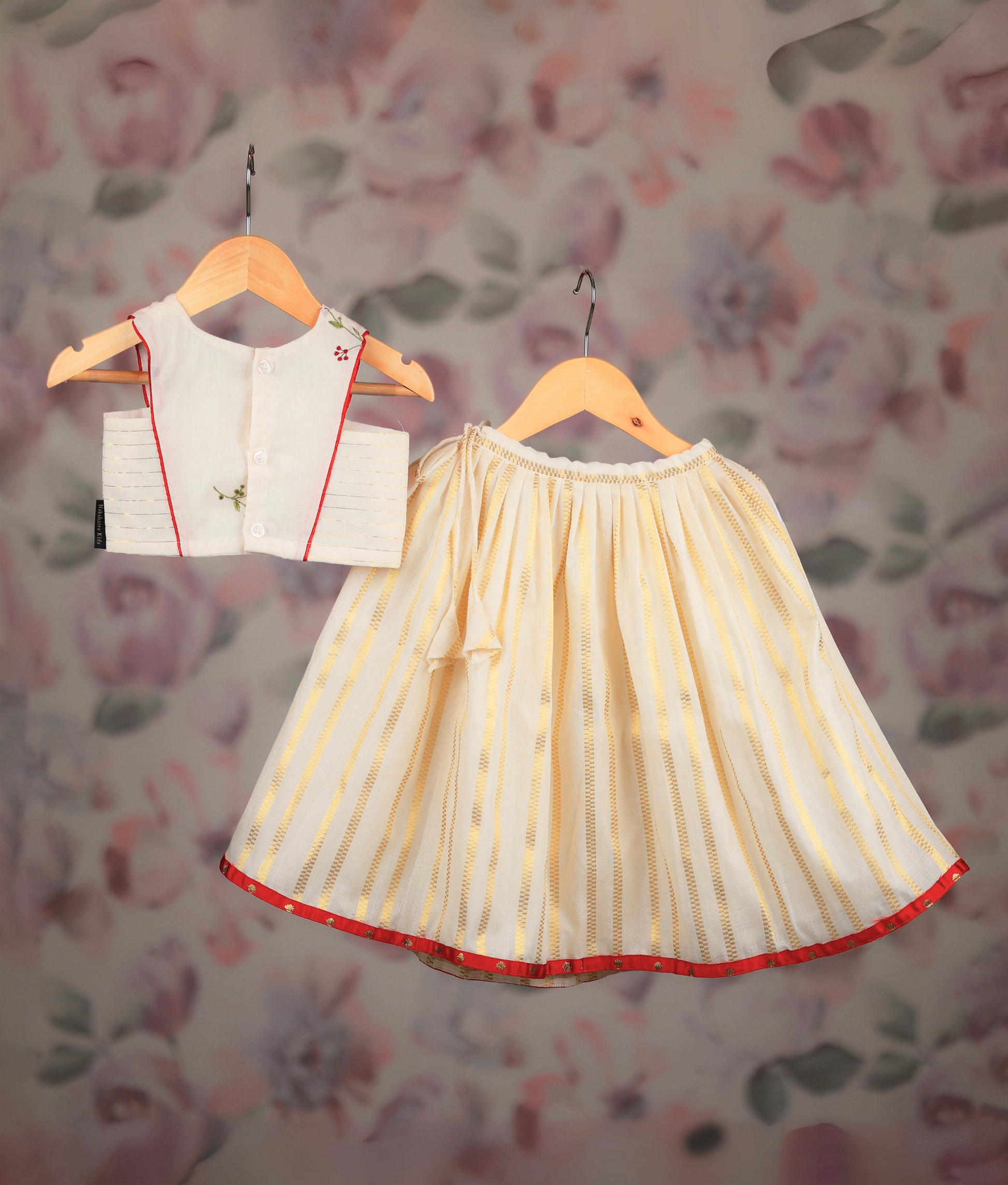 Back view of an off-white and golden baby girl skirt with embroidery top, displayed on hangers.