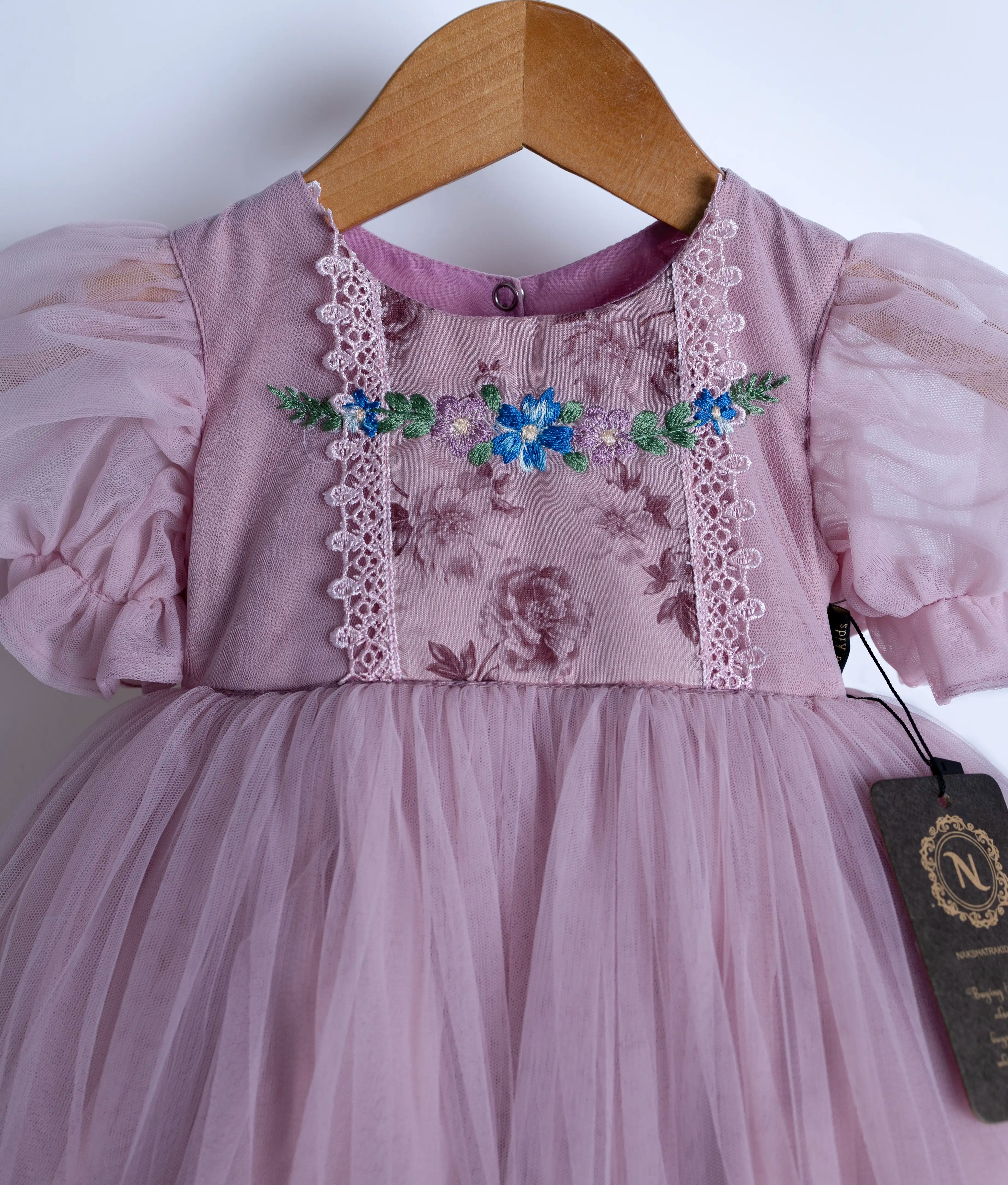Close view of an lavender floral embroidered frock with short puffed sleeves and multiple layers of tulle frills, displayed on a hanger.