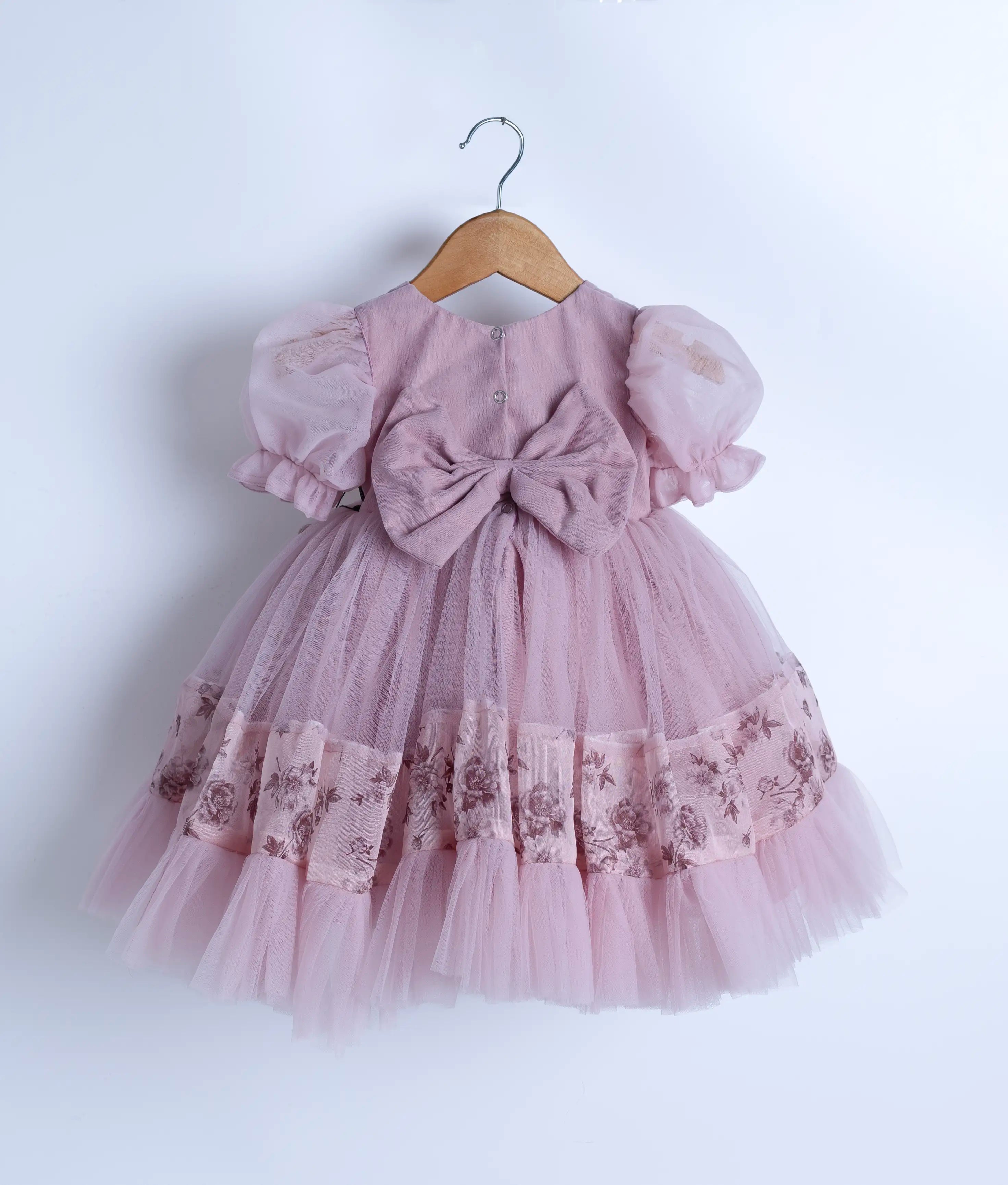 Back view of an lavender floral embroidered frock with short puffed sleeves and multiple layers of tulle frills, displayed on a hanger.