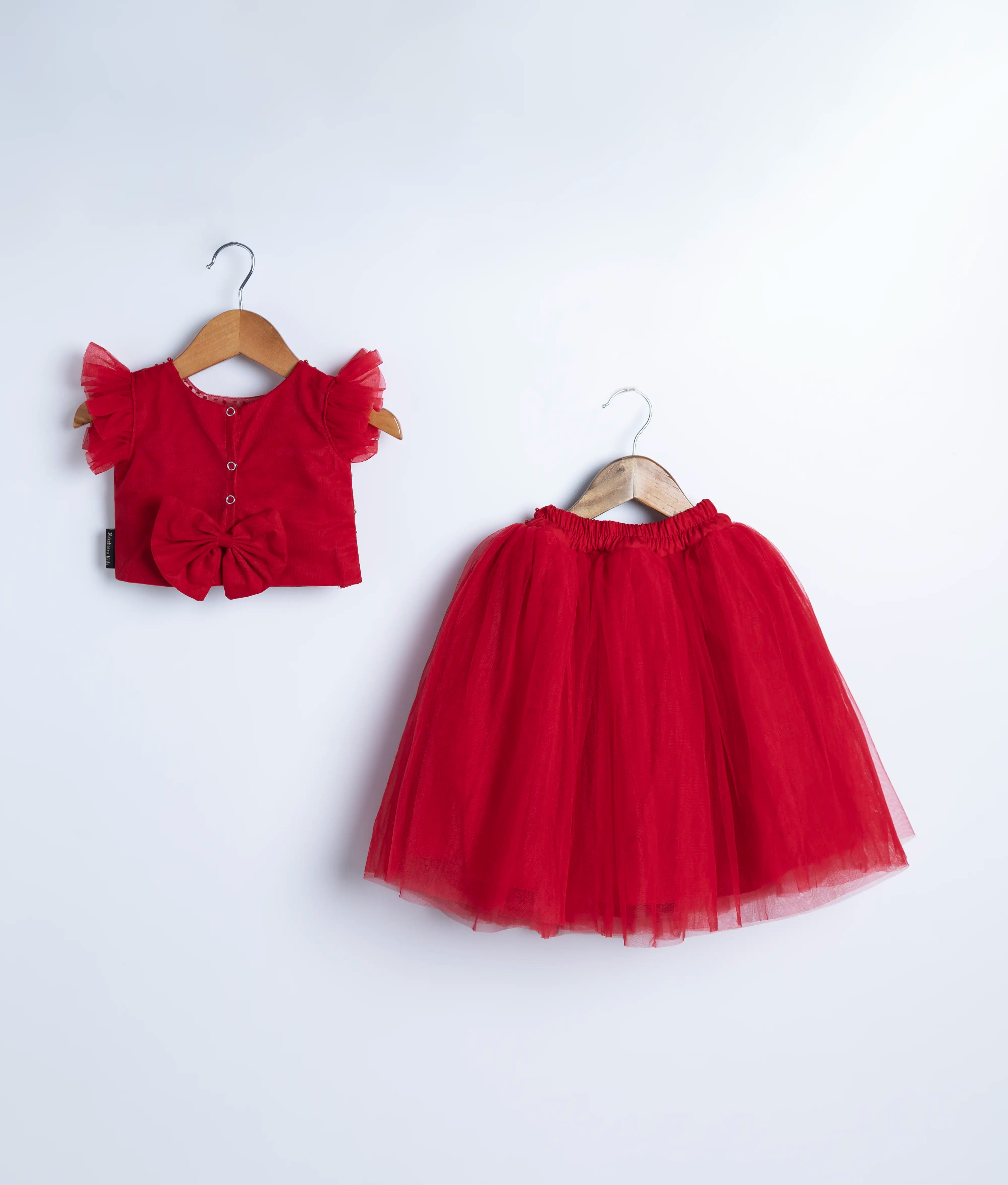 Back view of an red tulle net handworked crop top and skirt displayed on hangers against a white background.