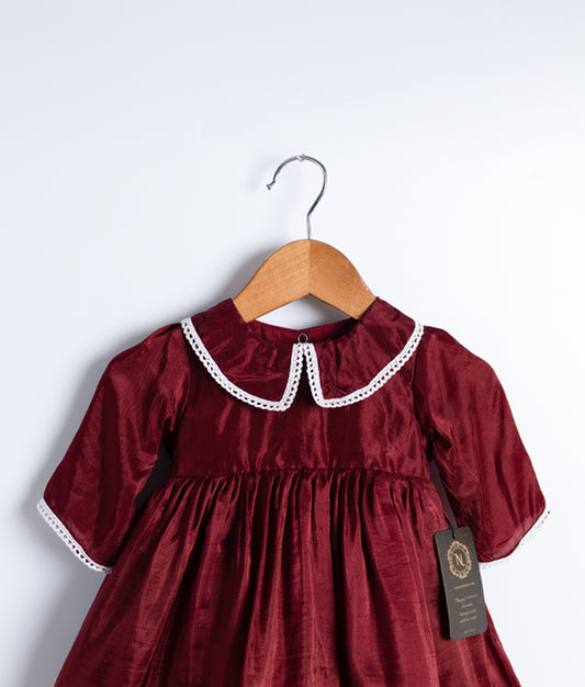Close view of an maroon christmas frock displayed on a hanger.
