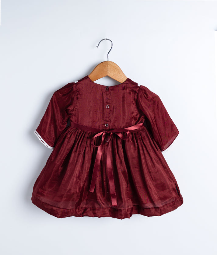 Back view of an maroon christmas frock displayed on a hanger.