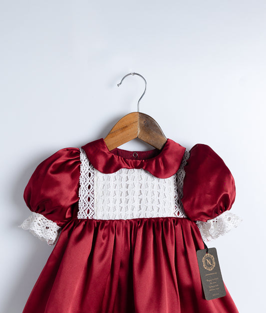 Close view of an maroon christmas frock with lace detailing and puff sleeves, displayed on a wooden hanger.