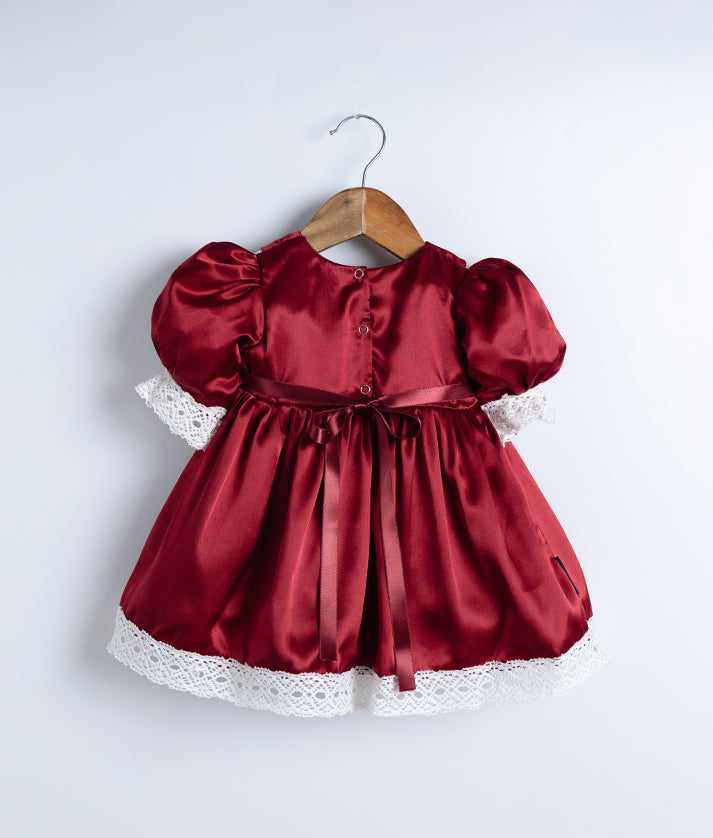 Back view of an maroon christmas frock with lace detailing and puff sleeves, displayed on a wooden hanger.
