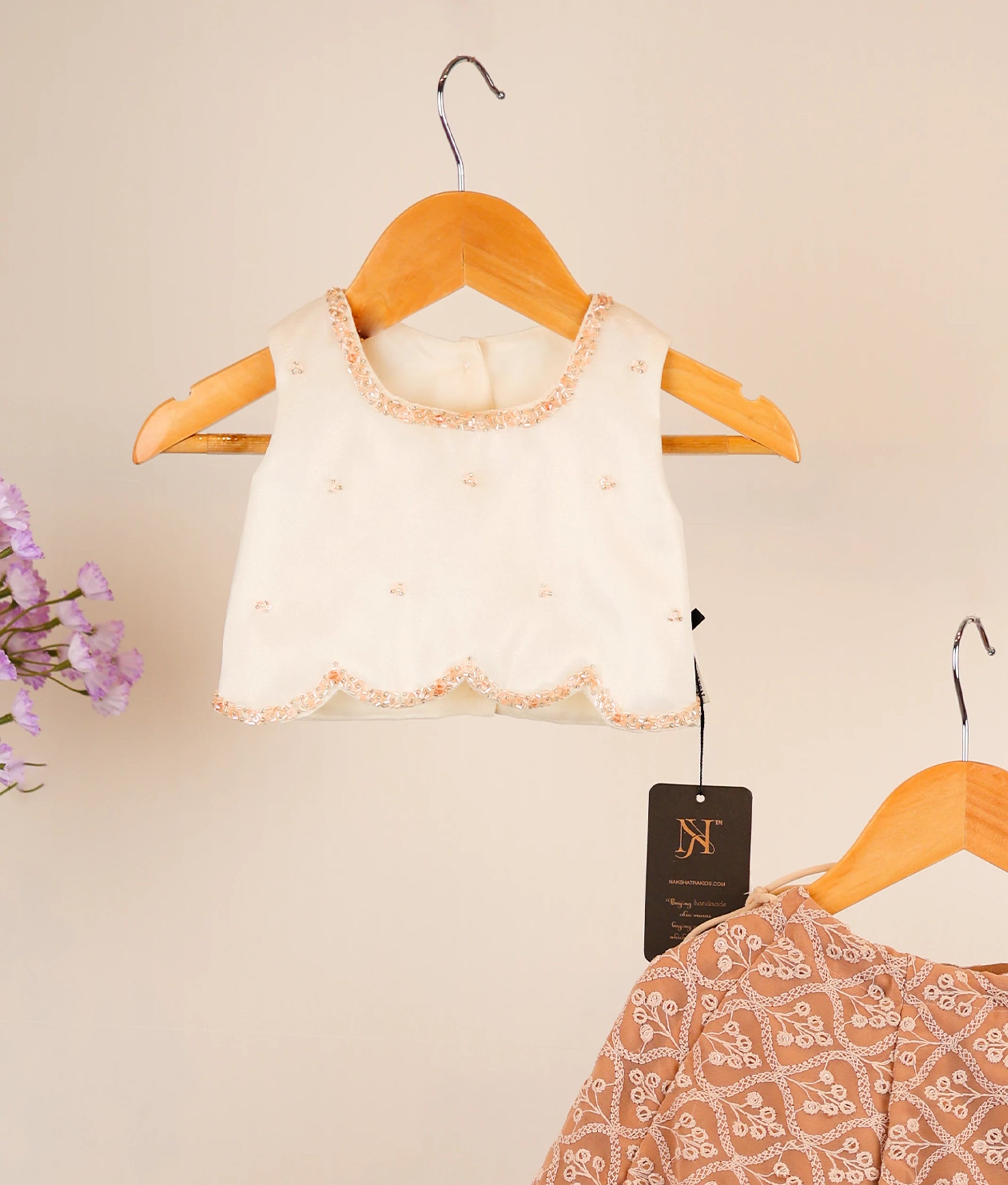 Close view off-white top and georgette skirt on hangers against a beige background