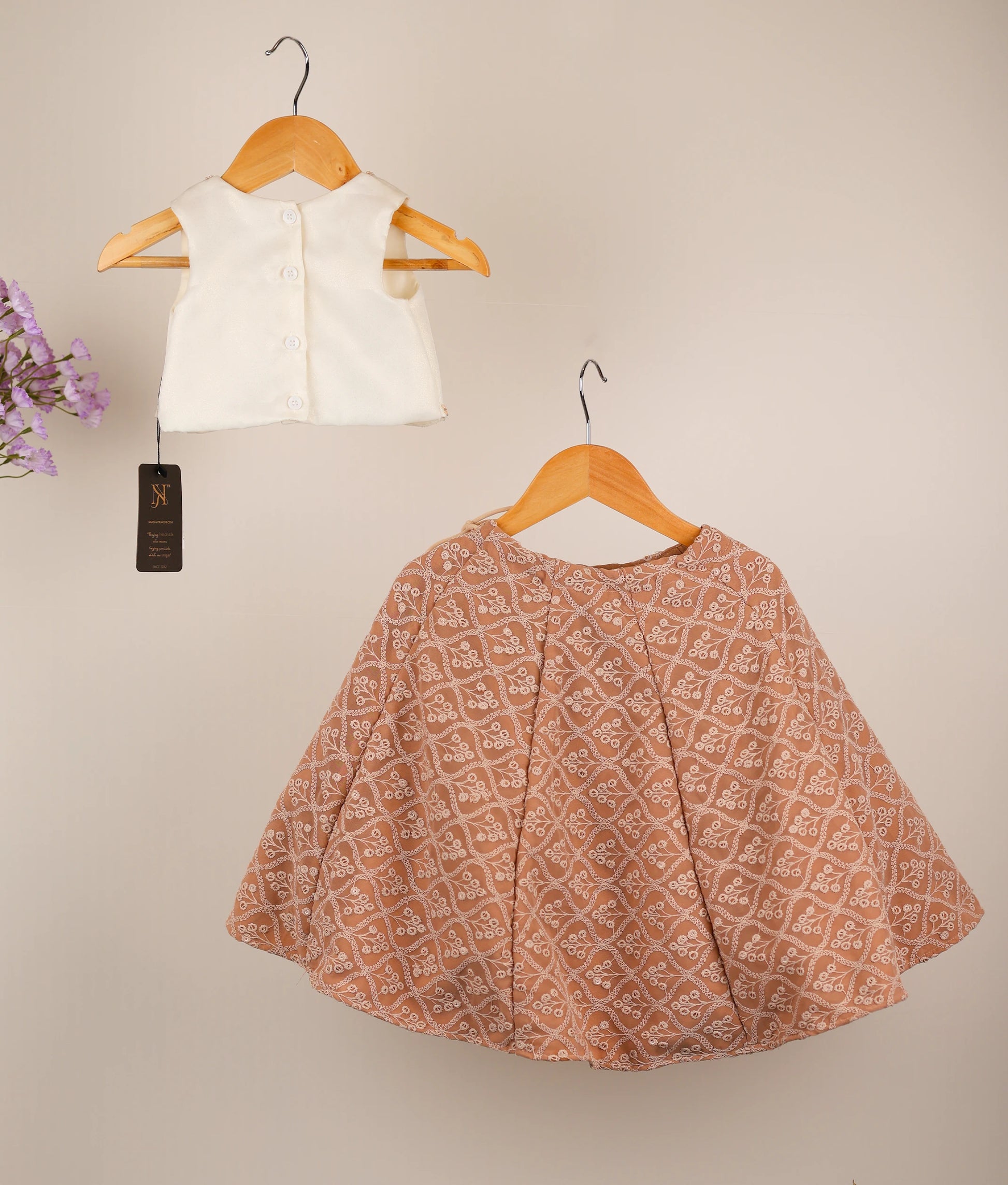 Back view an off-white top and georgette skirt on hangers against a beige background