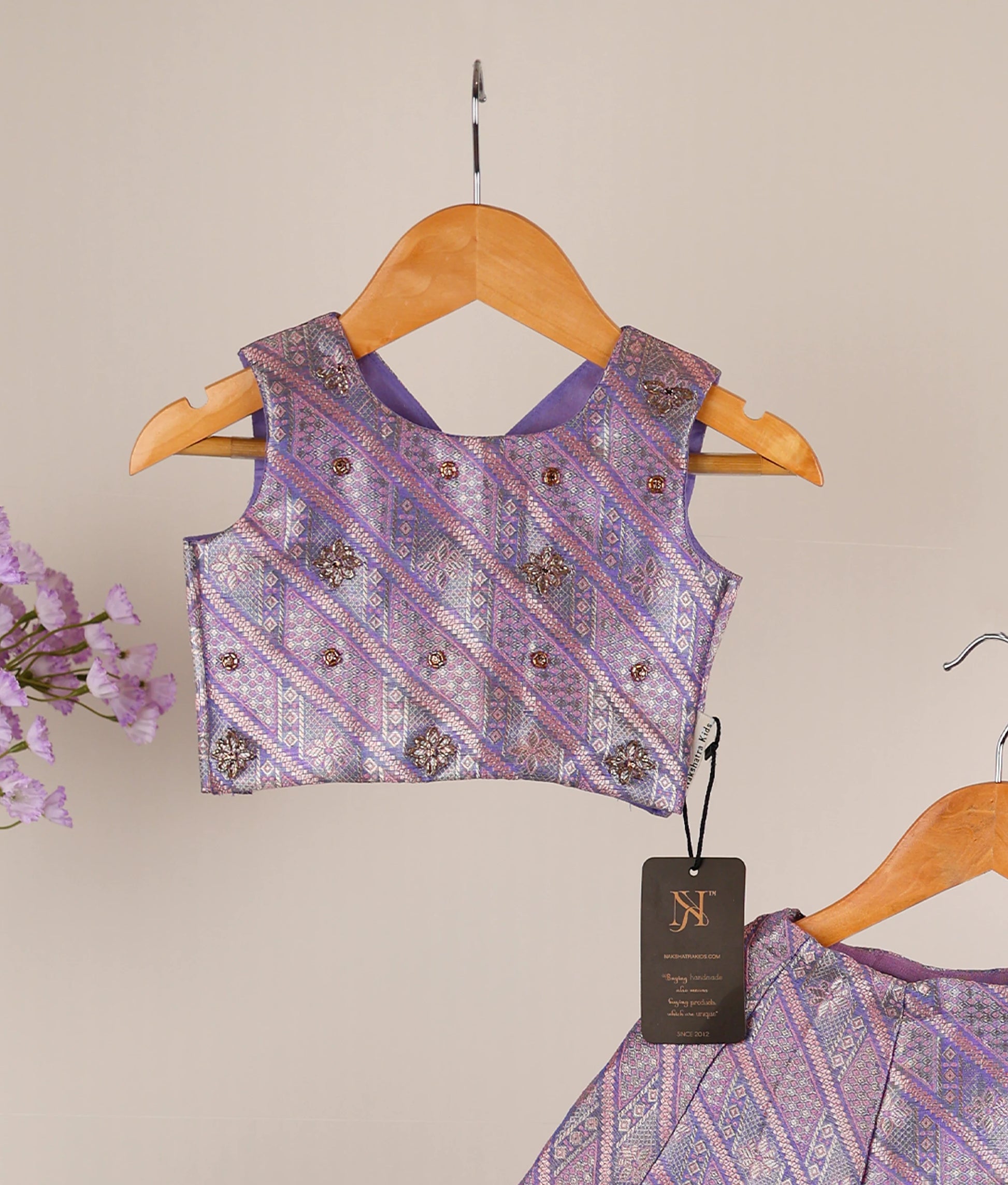 Close view of lavender traditional outfit with skirt and top on hangers against an ash background.