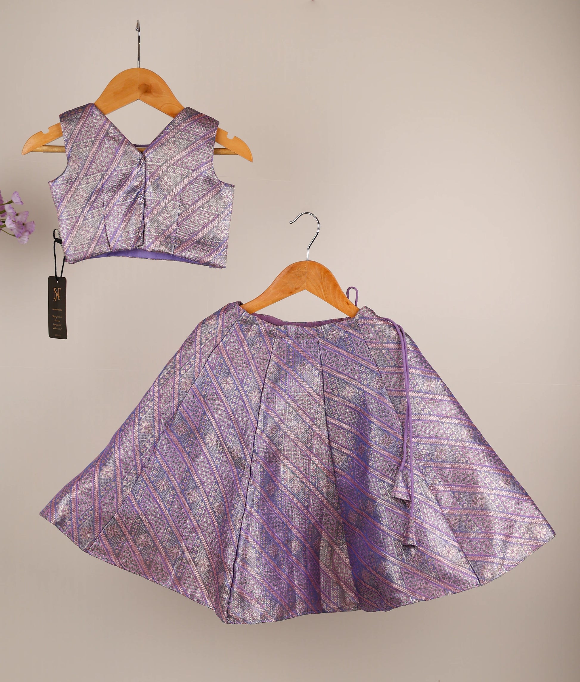 Back view of a traditional lavender outfit with skirt and top on hangers against an ash background.