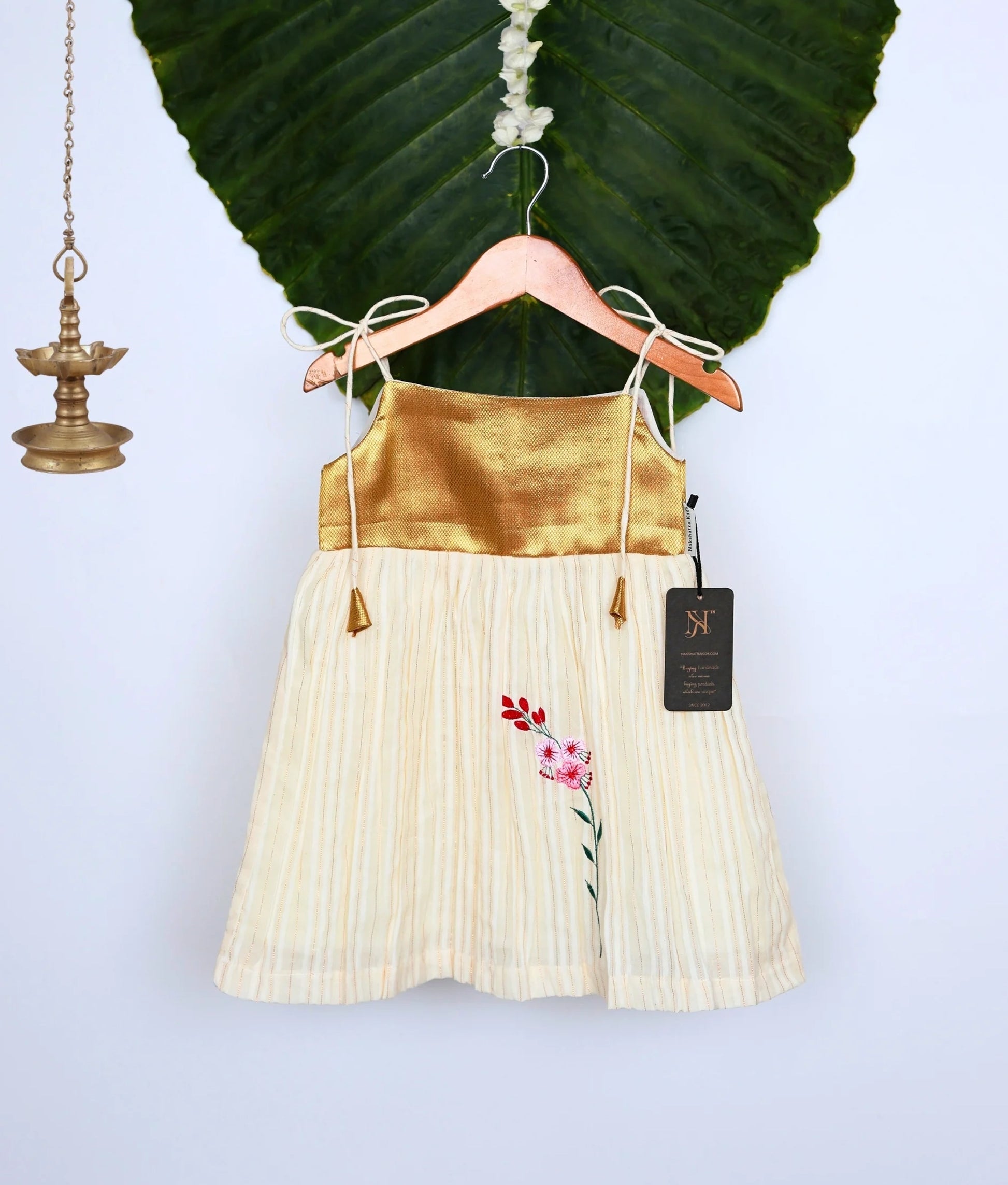 A golden and off-white frock on a hanger with a leafy background.