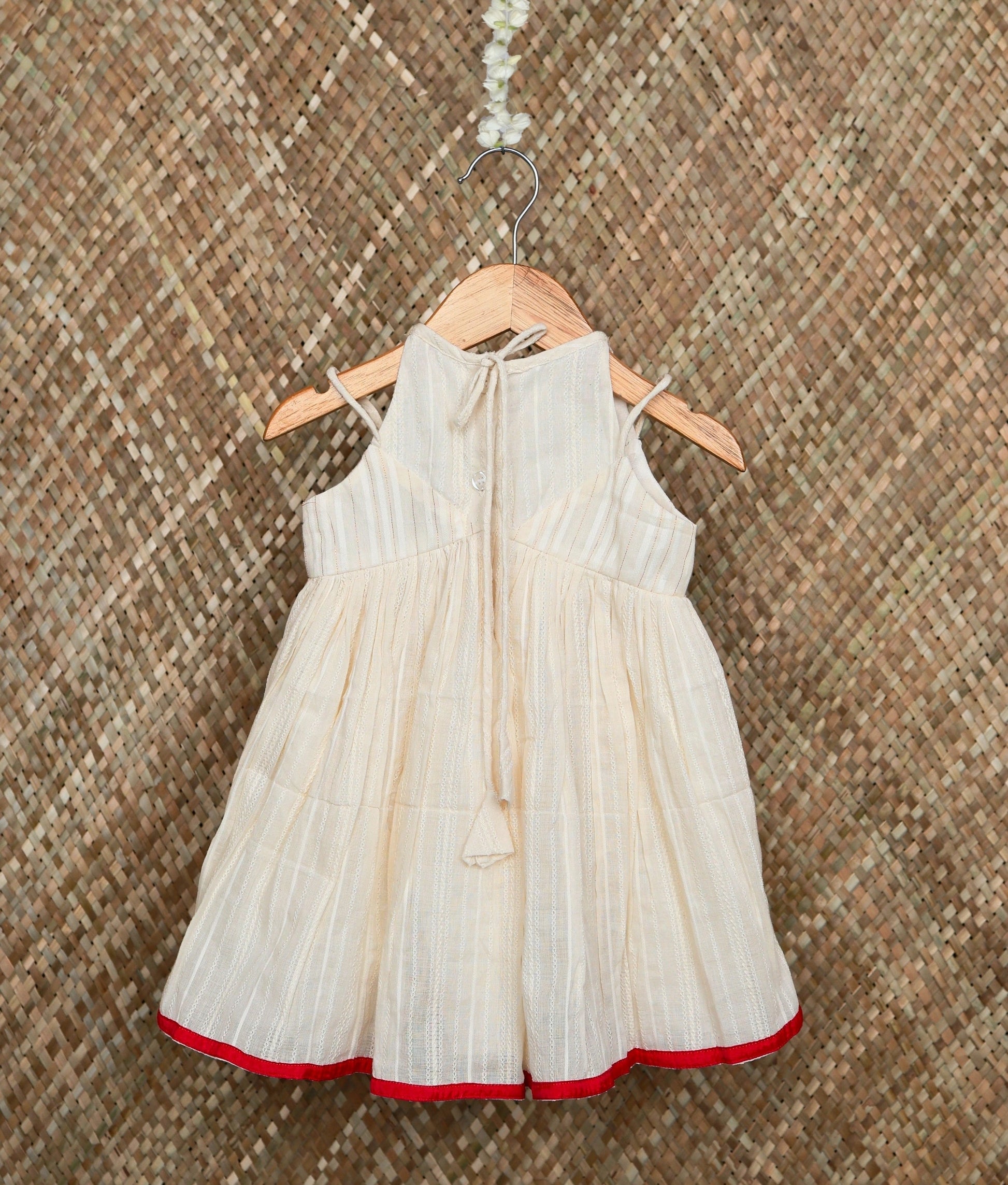 Back view of a traditional off-white baby girl dress with red floral embroidery and a red border, festive ethnic wear.